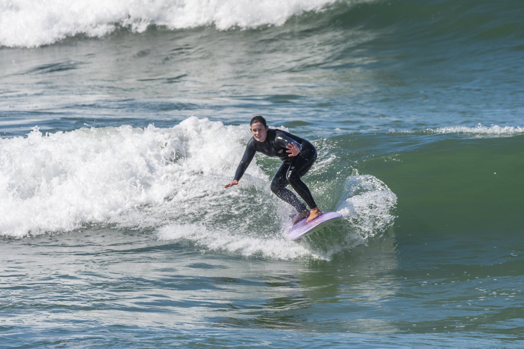 Person surfing on ocean wave, wearing black wetsuit and riding a purple surfboard. Porto Surf Femmes,  photography by Abilio Meneses