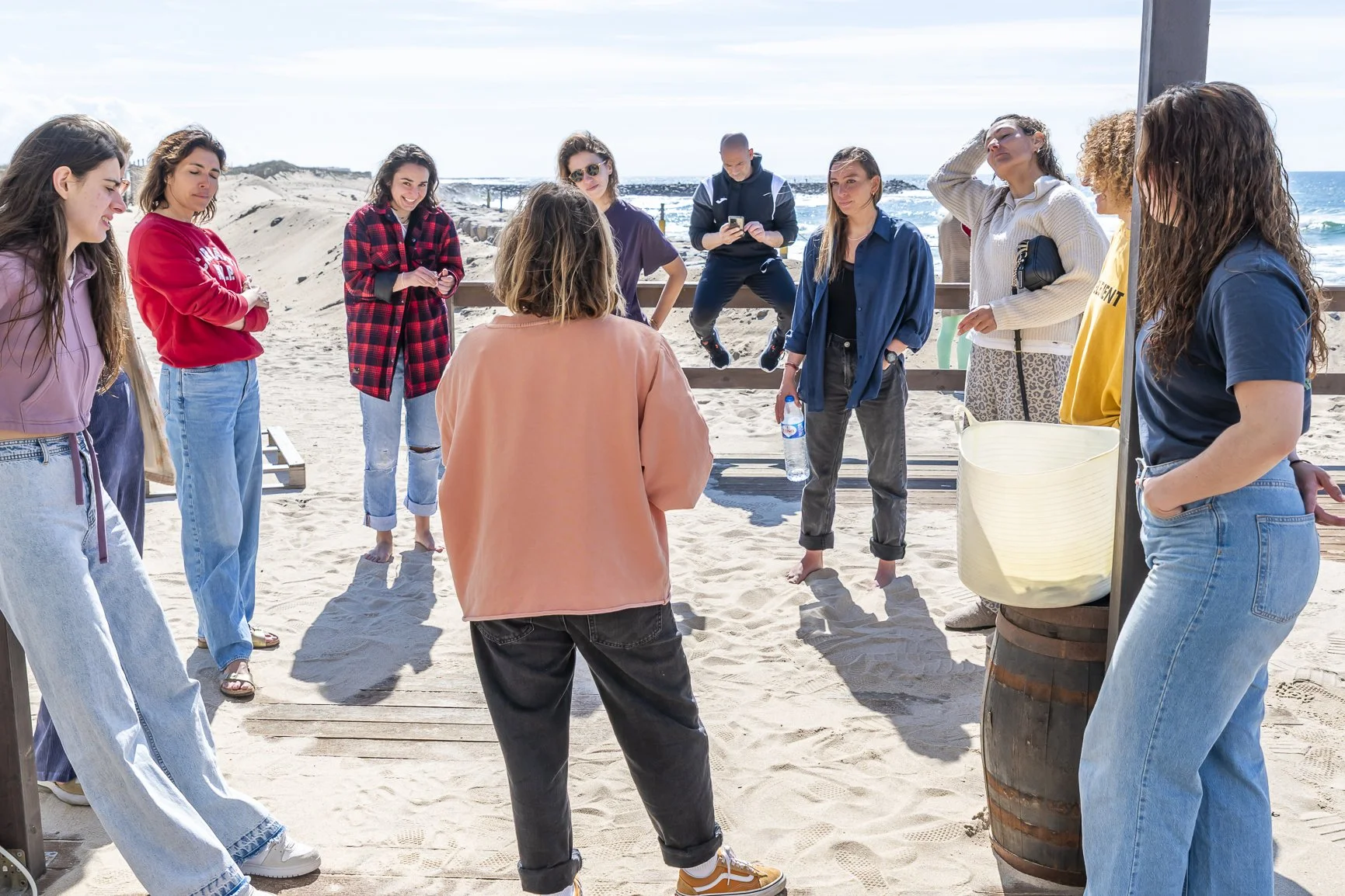 Group of women standing and talking on a sandy beach with ocean in the background. Porto Surf Femmes. Photography by Abilio Meneses