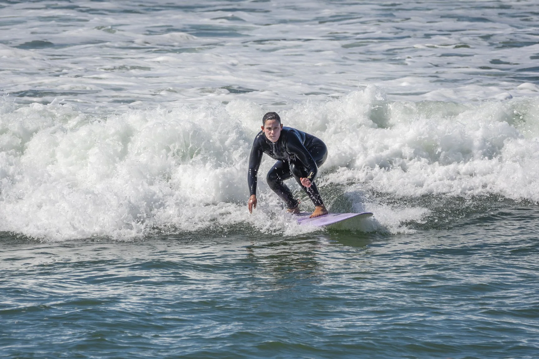 Person surfing on a wave with a purple surfboard, wearing a black wetsuit in the ocean. Porto Surf Femmes,  photography by Abilio Meneses
