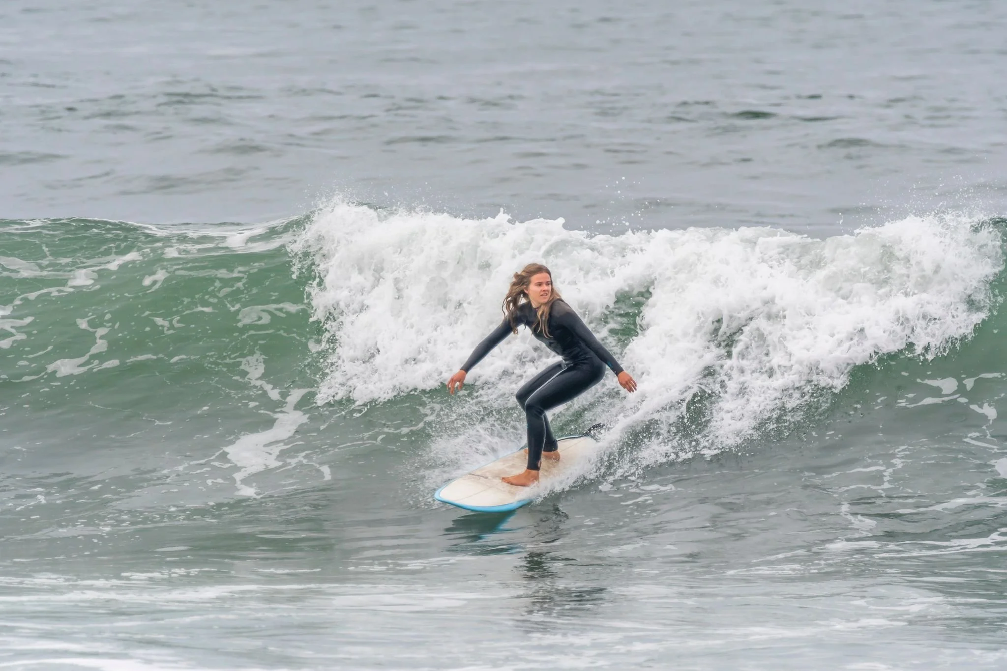 A person surfing on a wave in the ocean, wearing a black wetsuit. Porto Surf Femmes,  photography by Abilio Meneses