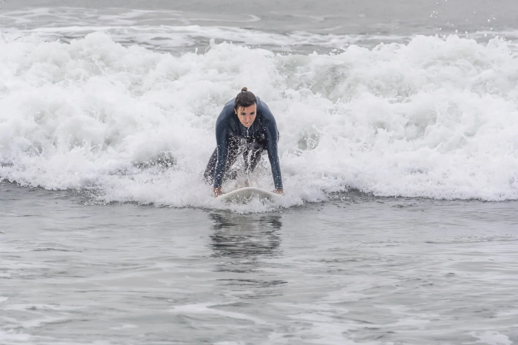 Person on a surfboard riding a wave in the ocean, wearing a wetsuit, with white foamy water around them. Porto Surf Femmes,  photography by Abilio Meneses