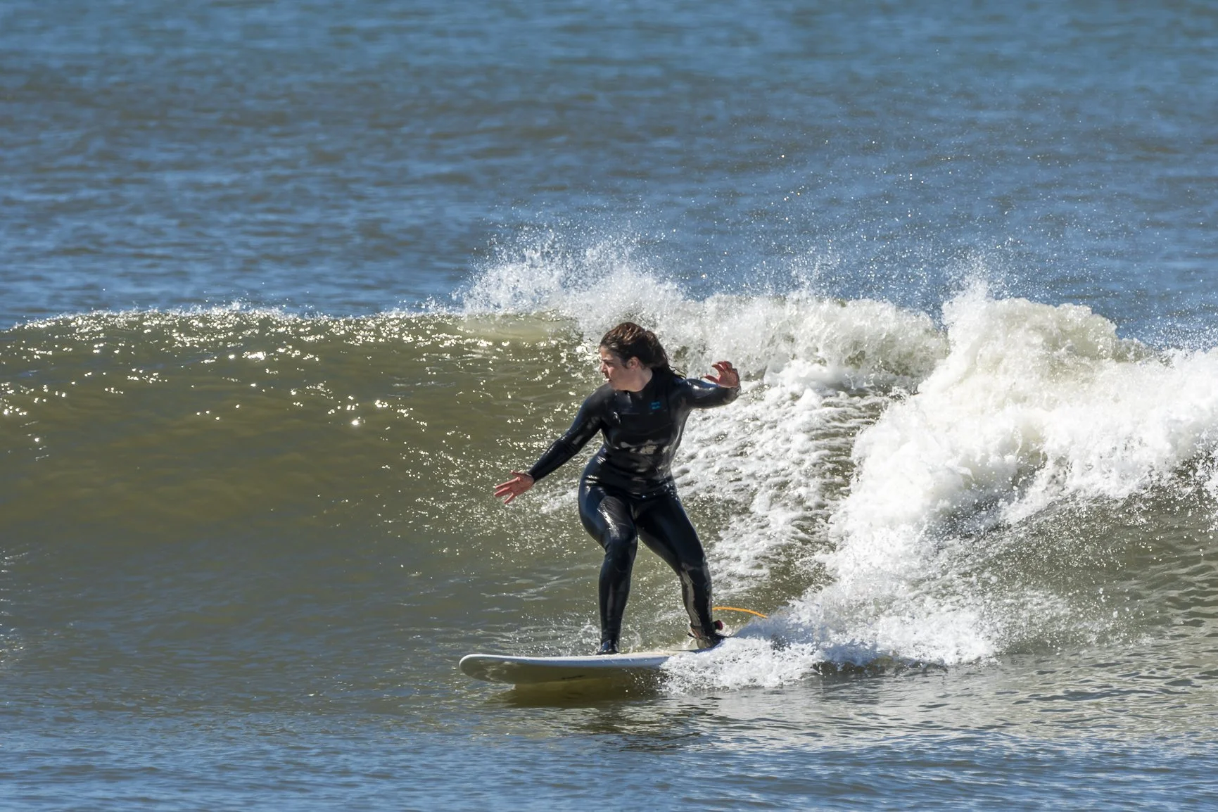 Woman  surfing on a wave in the ocean, wearing a black wetsuit, with water splashing around. Porto Surf Femmes. Photography by Abilio Meneses