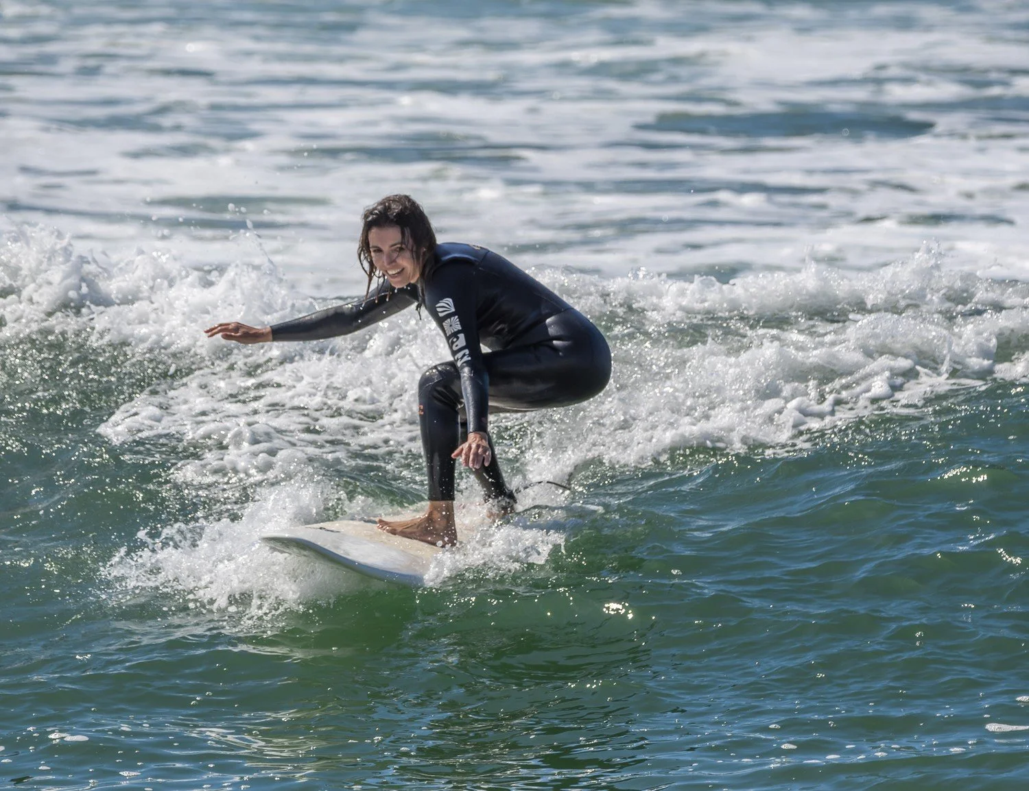 Person surfing on a wave, wearing a black wetsuit, in sunny weather. Porto Surf Femmes,  photography by Abilio Meneses