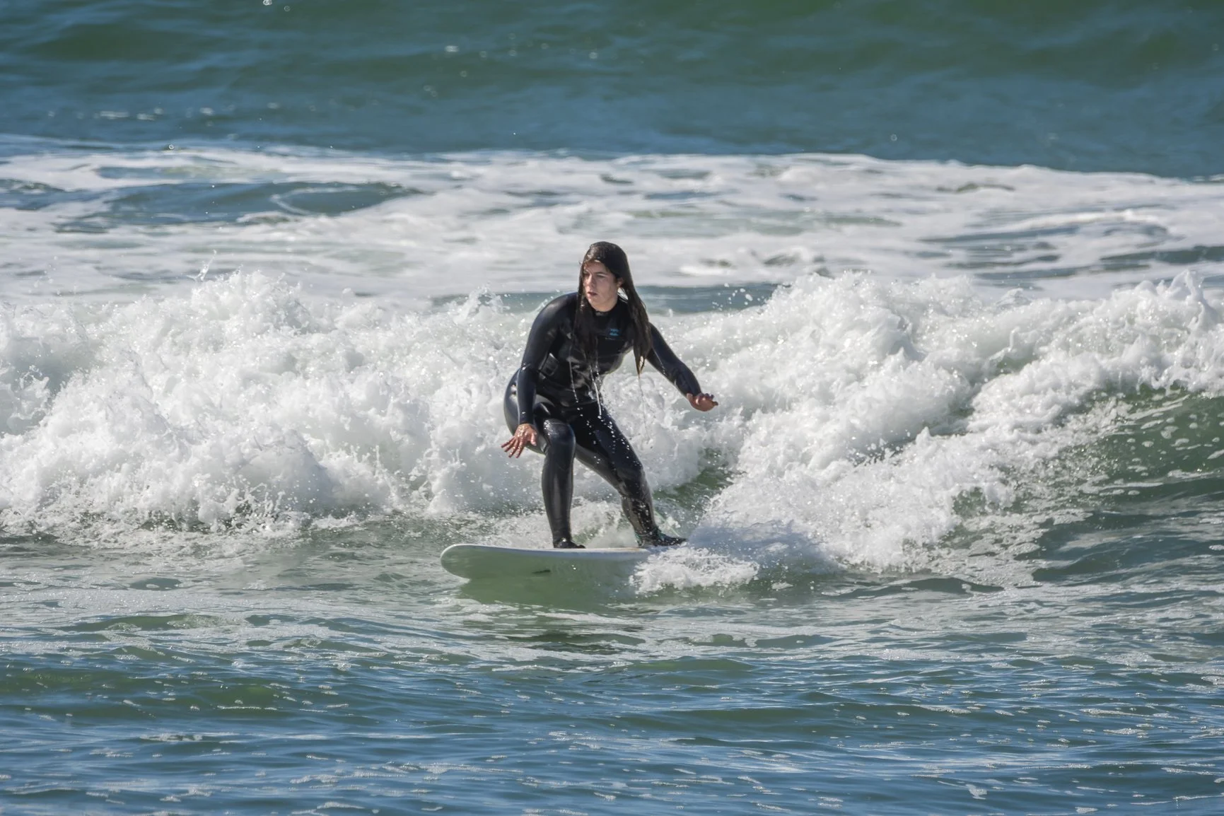 Person surfing on a small wave in the ocean, wearing a black wetsuit. Porto Surf Femmes,  photography by Abilio Meneses