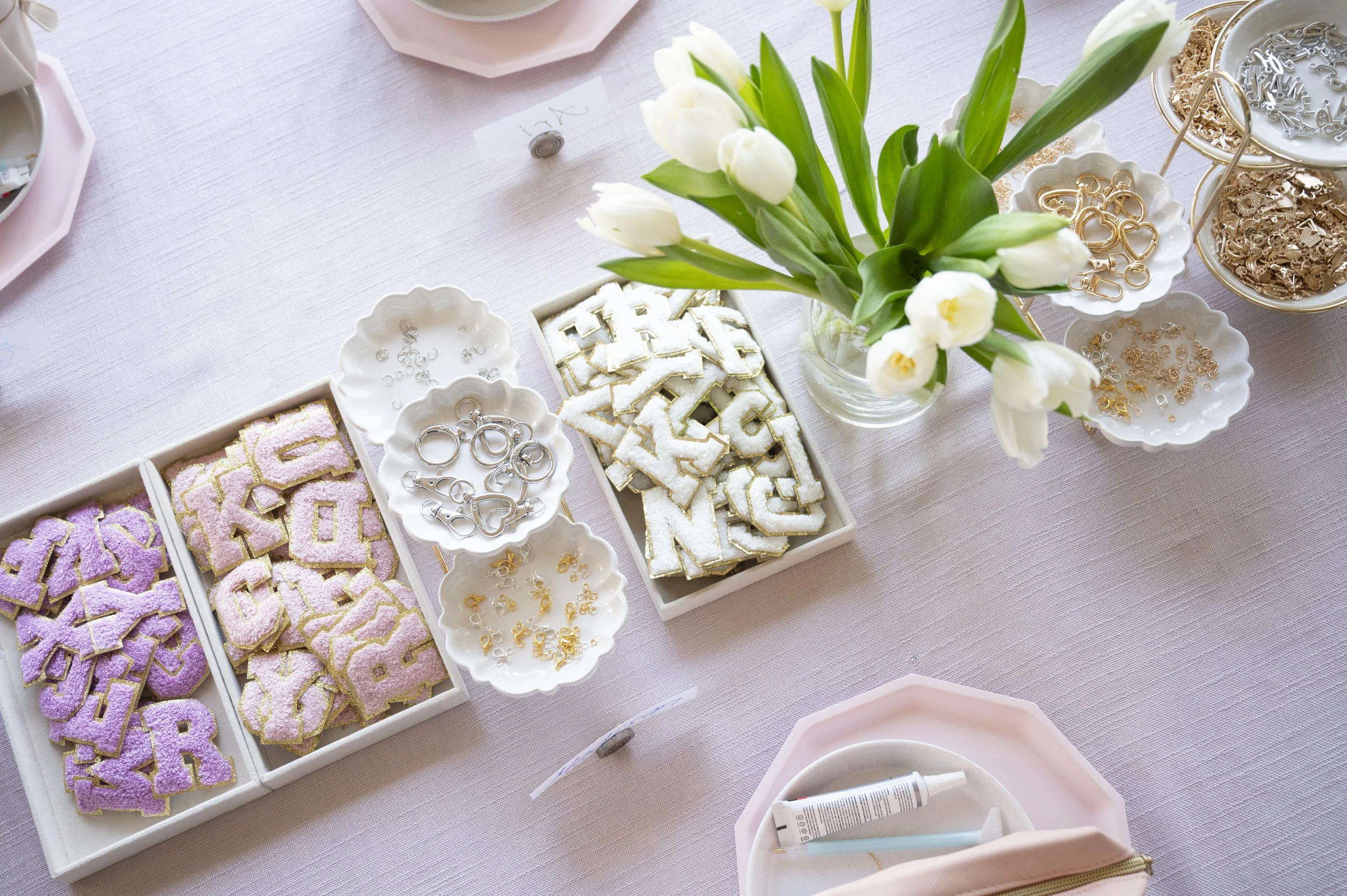 Table setting with pink glasses, a pink heart-shaped paper, and gold utensils. Beside the table, a pink pillow and a decorative fairy wing with floral embroidery are visible.