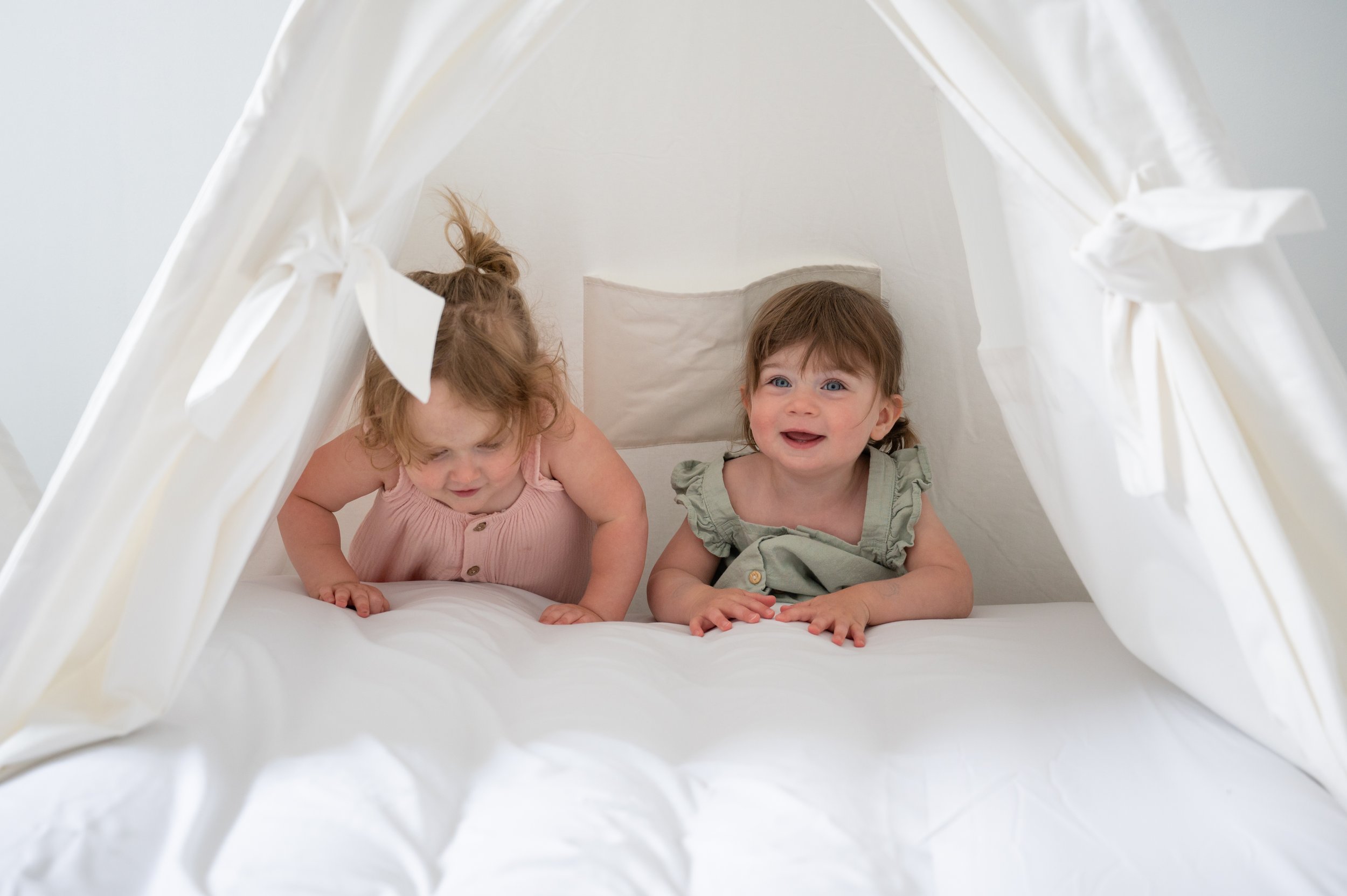 two young girls smiling as they play in a white tent