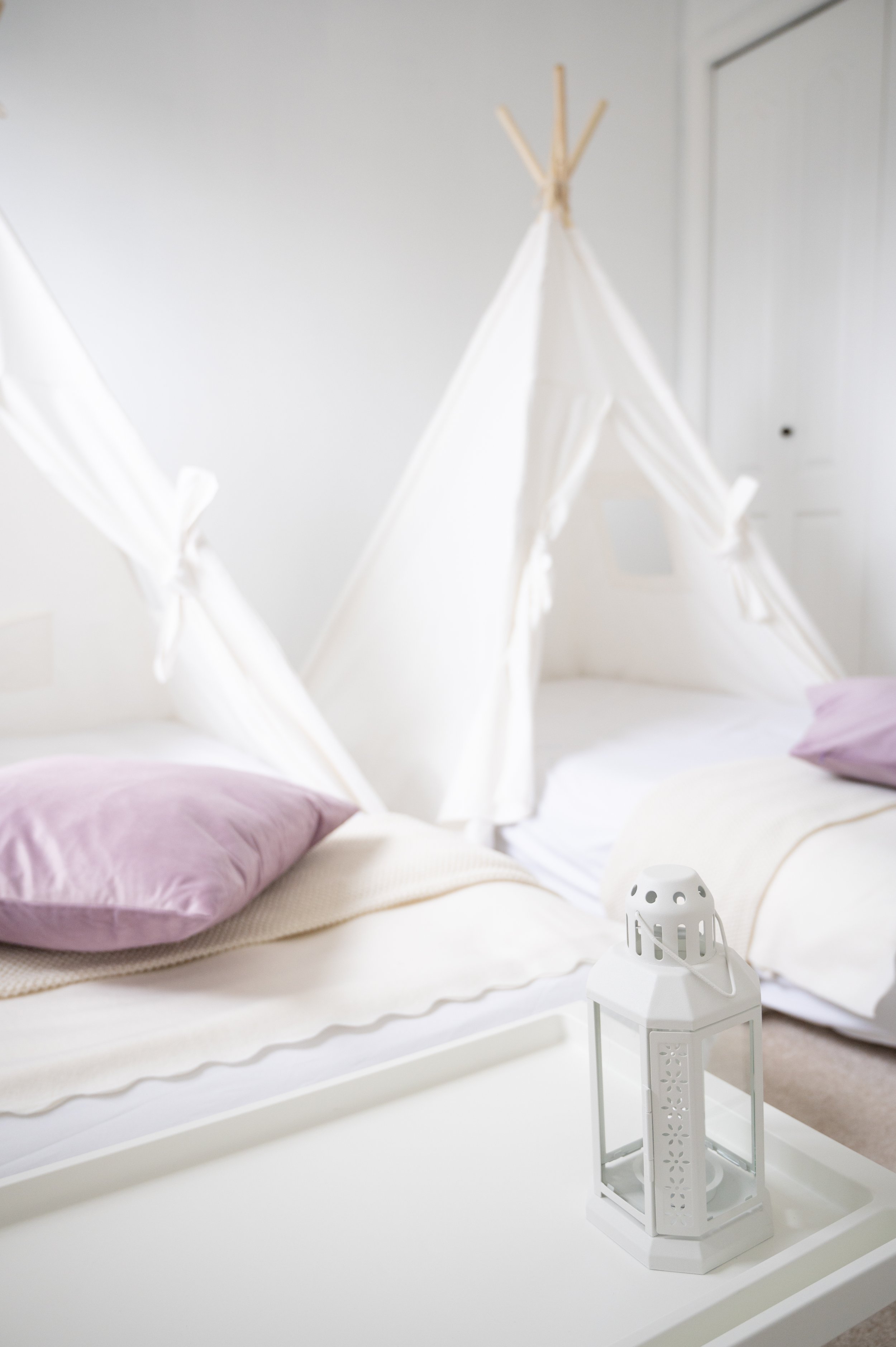 Two beds with pink pillows, a white tray, and a white lantern in a room with a white teepee tent in the background.