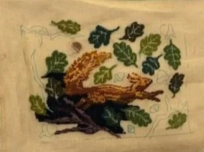 Embroidery of a bird perched on a branch with green leaves.