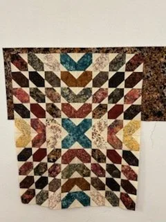 Colorful quilt with geometric patterns in various shades including blue, red, yellow, brown, and white, arranged symmetrically.