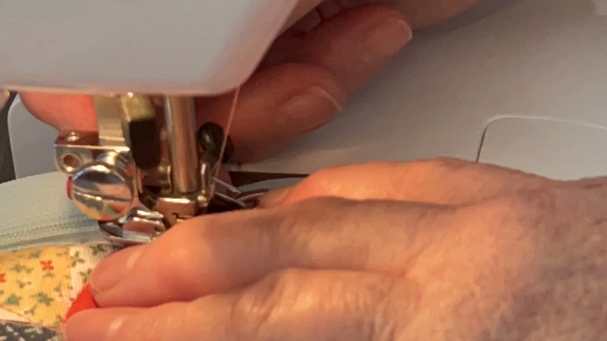 Close-up of hands guiding fabric through a sewing machine needle, with colorful thread and fabric being sewn.