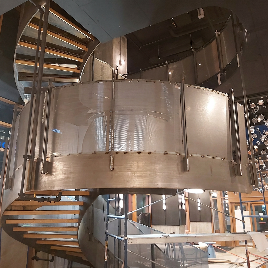Gros plan architectural mettant en valeur la finition épurée de l'acier brut sous une couche de laque claire protectrice sur la structure d'un escalier d'hôtel.