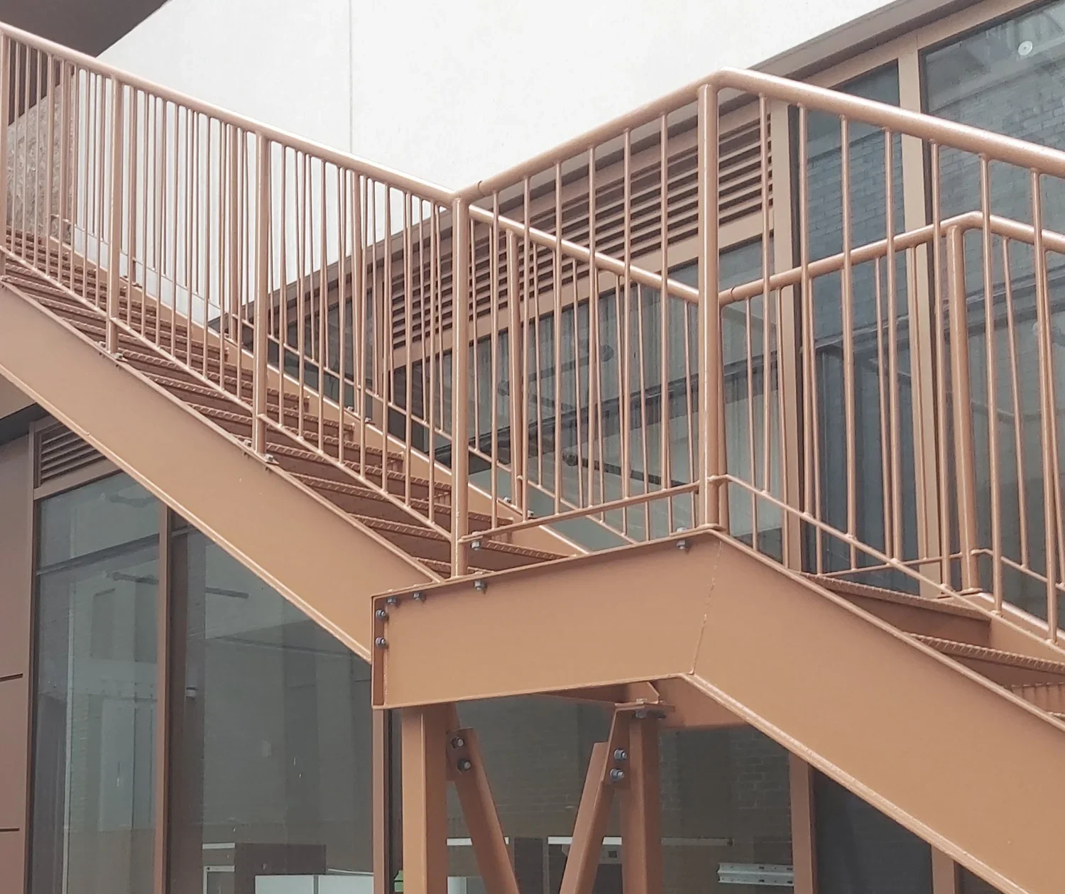 Gros plan architectural sur les raccordements boulonnés, les garde-corps et la finition protectrice cuivrée d'un escalier de secours commercial.