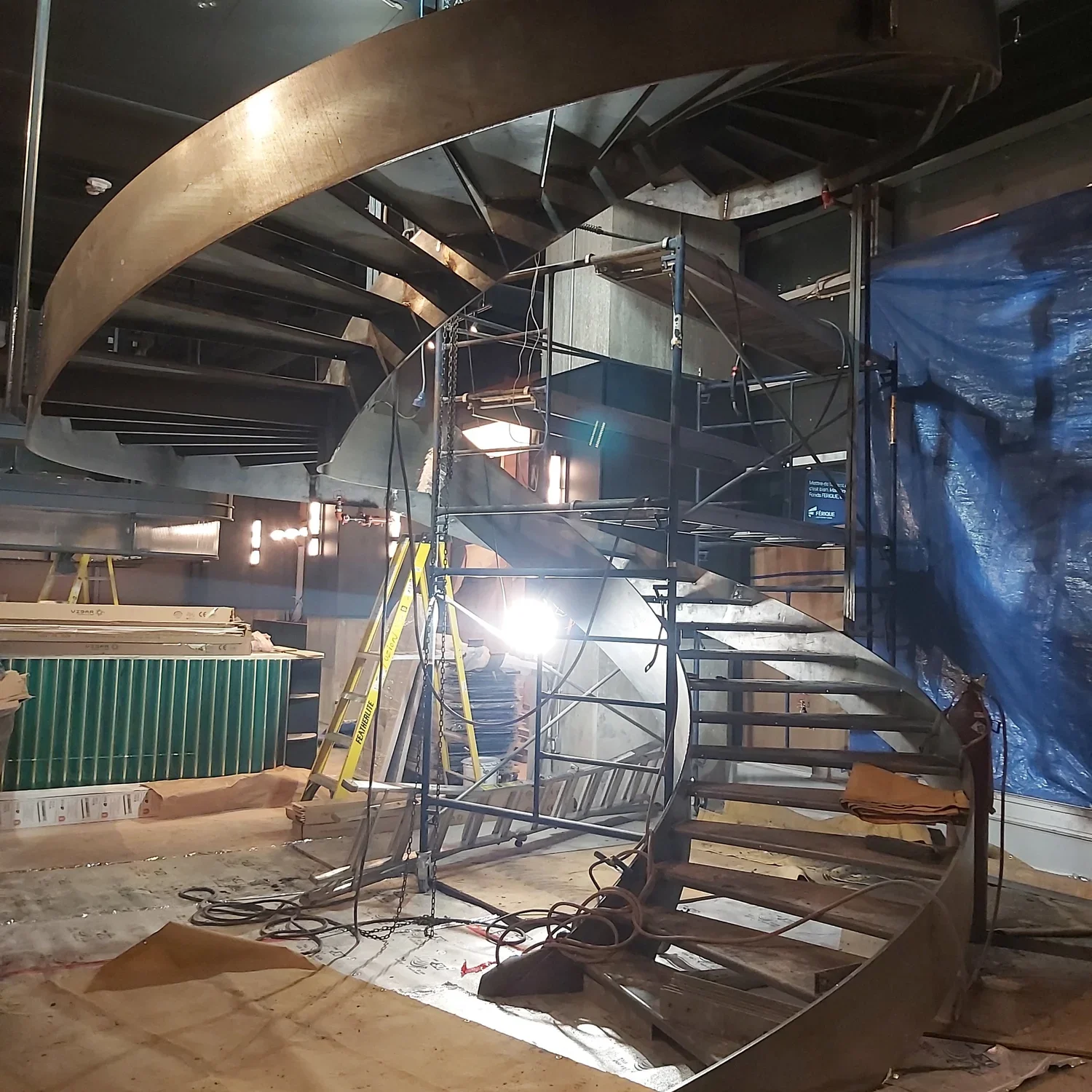 Structure d'un grand escalier hélicoïdal en acier brut en cours d'assemblage et d'installation sur le chantier d'un hall d'hôtel.