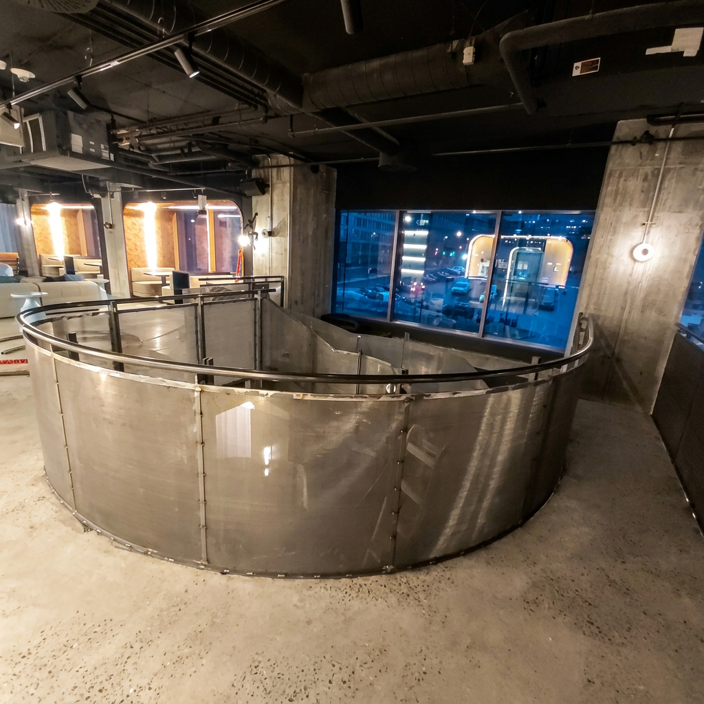 Section en demi-cercle d'un garde-corps en métal ouvré au fini laque claire, délimitant l'espace sur un plancher de béton.