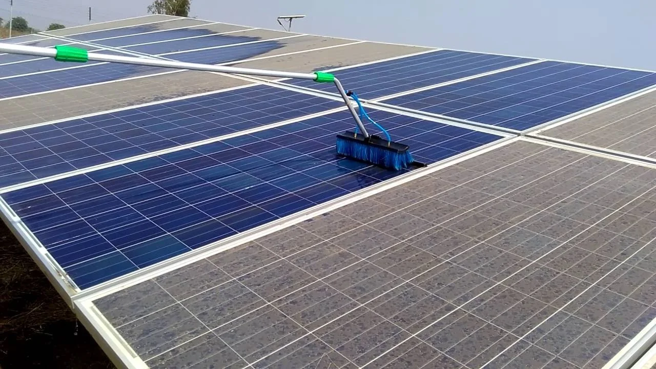 Cleaning solar panels on a rooftop using a brush attached to a long pole.