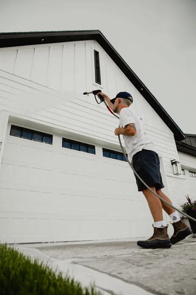 A man cleaning the exterior window of a white garage door using a spray nozzle.