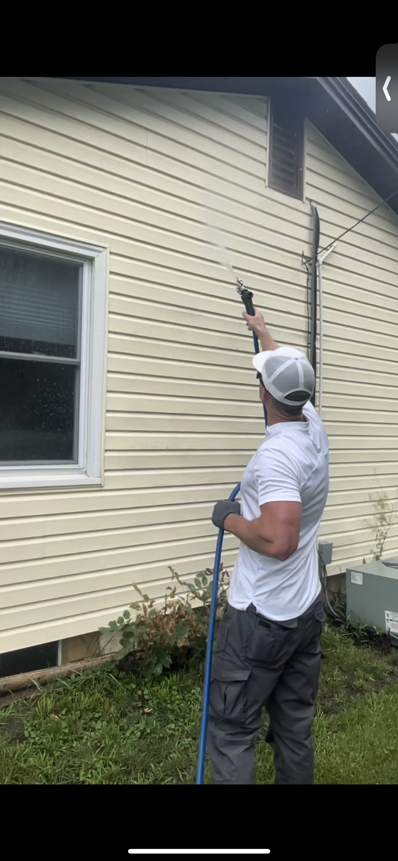 Man power washing the exterior siding of a house with a high-pressure washer.