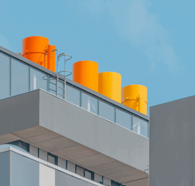 Modern building rooftop with colorful orange and yellow ventilation pipes against blue sky.