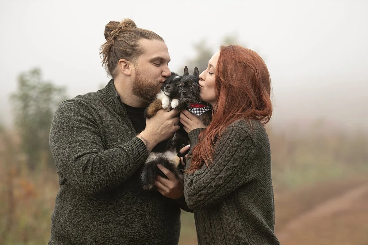 Family portraits of Brian Larson and his girlfriend with their two dogs at Garrard Landing Park, Marietta, Georgia, photographed outdoors with natural lighting in Christmas sweaters for holiday cards by Caitlin Tabilog of Atlanta Portrait Co.