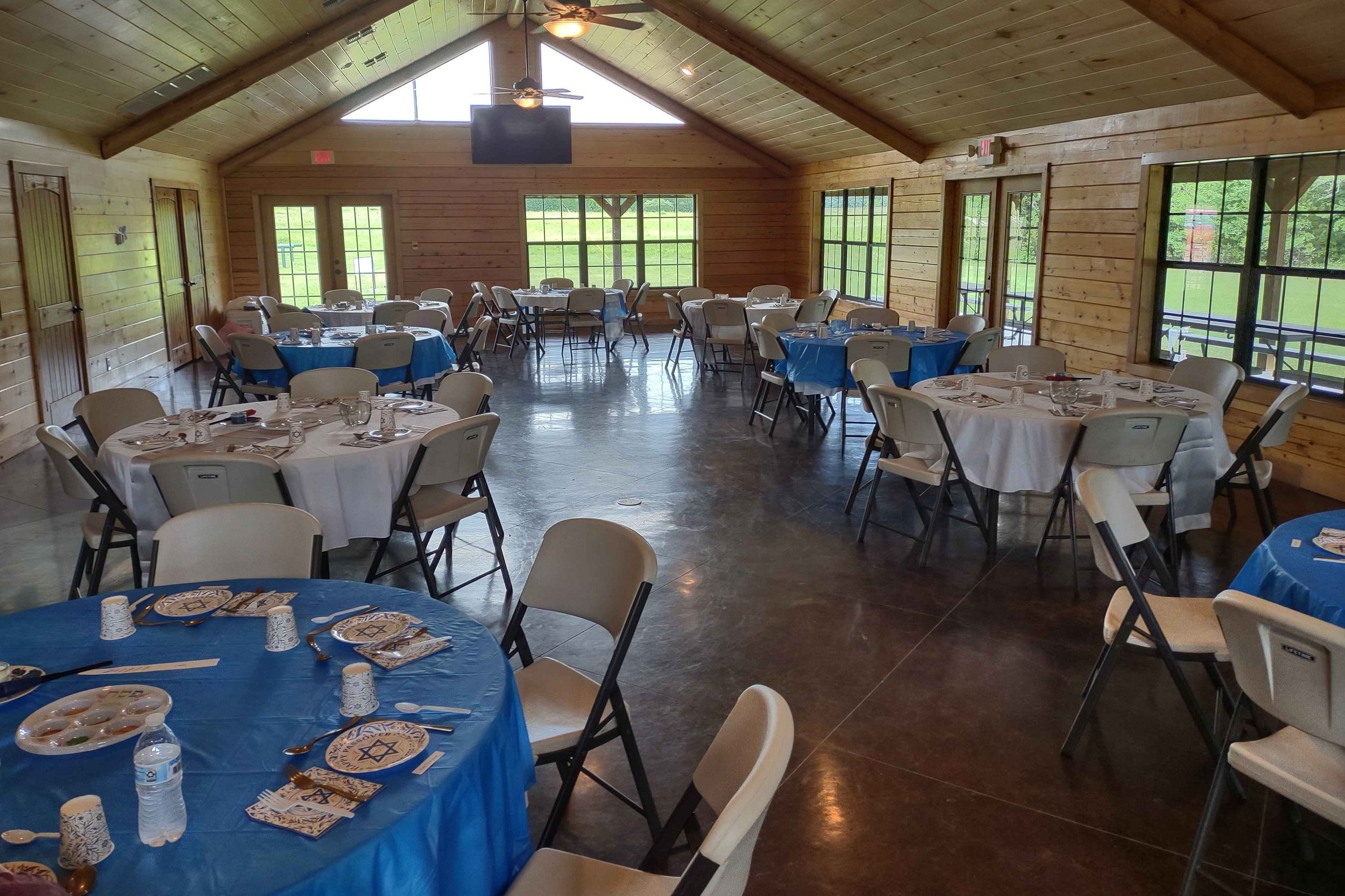 Banquet hall with round tables covered in blue and white tablecloths, set with plates, silverware, glasses, and napkins, arranged for a Jewish celebration.