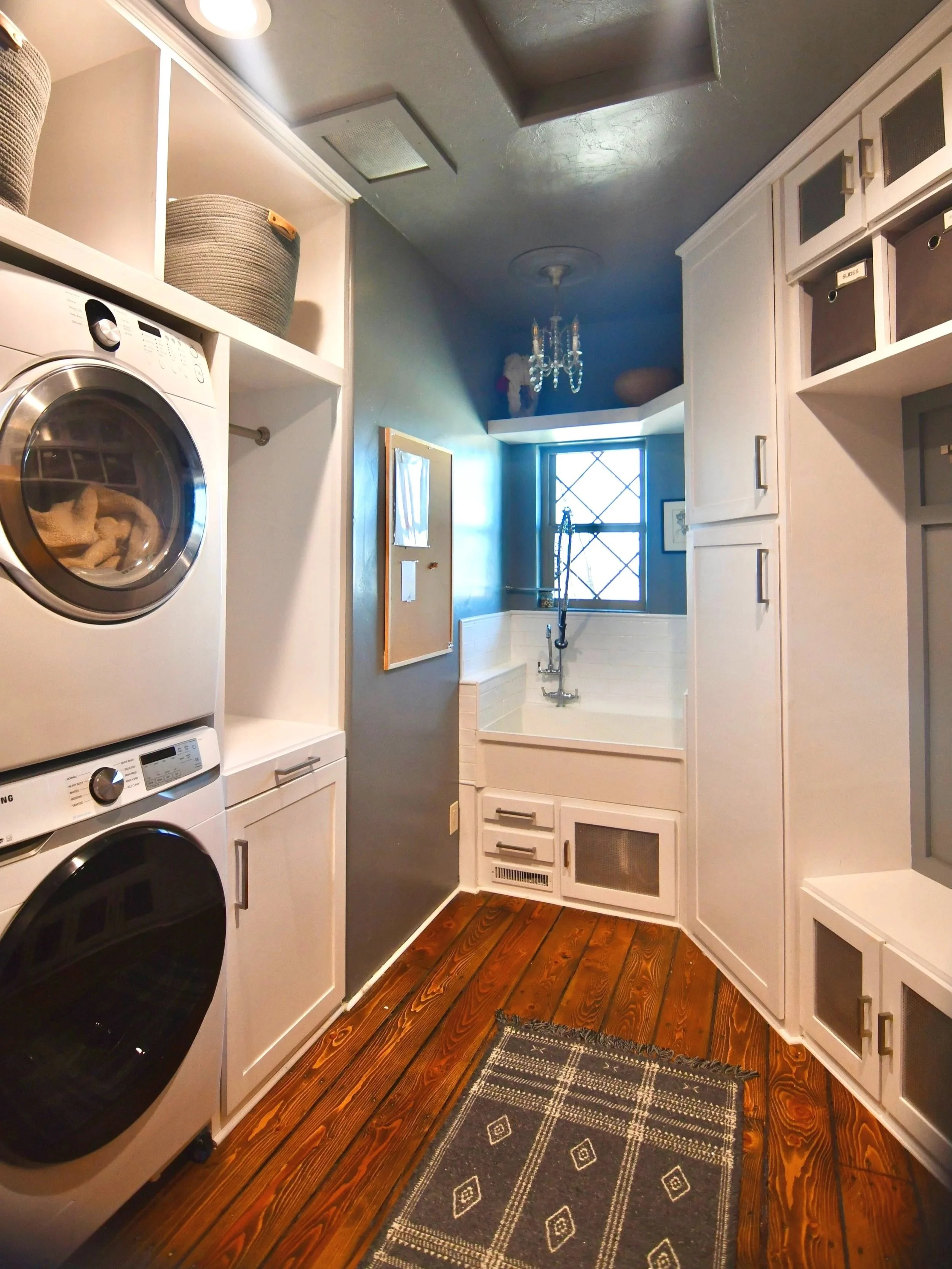 Laundry room with washer and dryer on the left, white cabinetry and wood flooring, and a small bathtub at the back near a window.