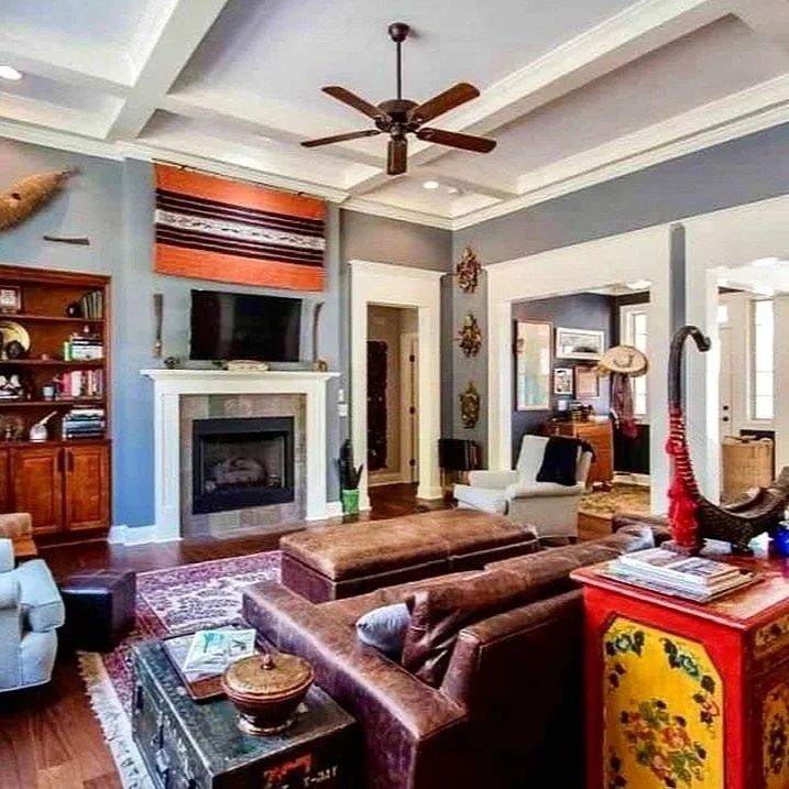 Living room with blue walls, white trim, brown furniture, a fireplace, mounted TV, ceiling fan, and various decorations.