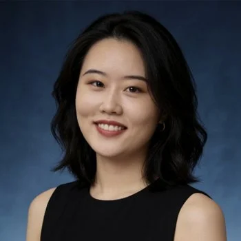 A smiling young woman smiles in front of a formal portrait background.