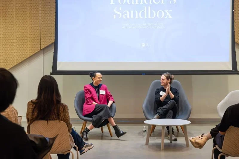 Ashleigh Axios participates in a seated conversation with another speaker at a Founder’s Sandbox event, engaging in dialogue on stage with an audience present.