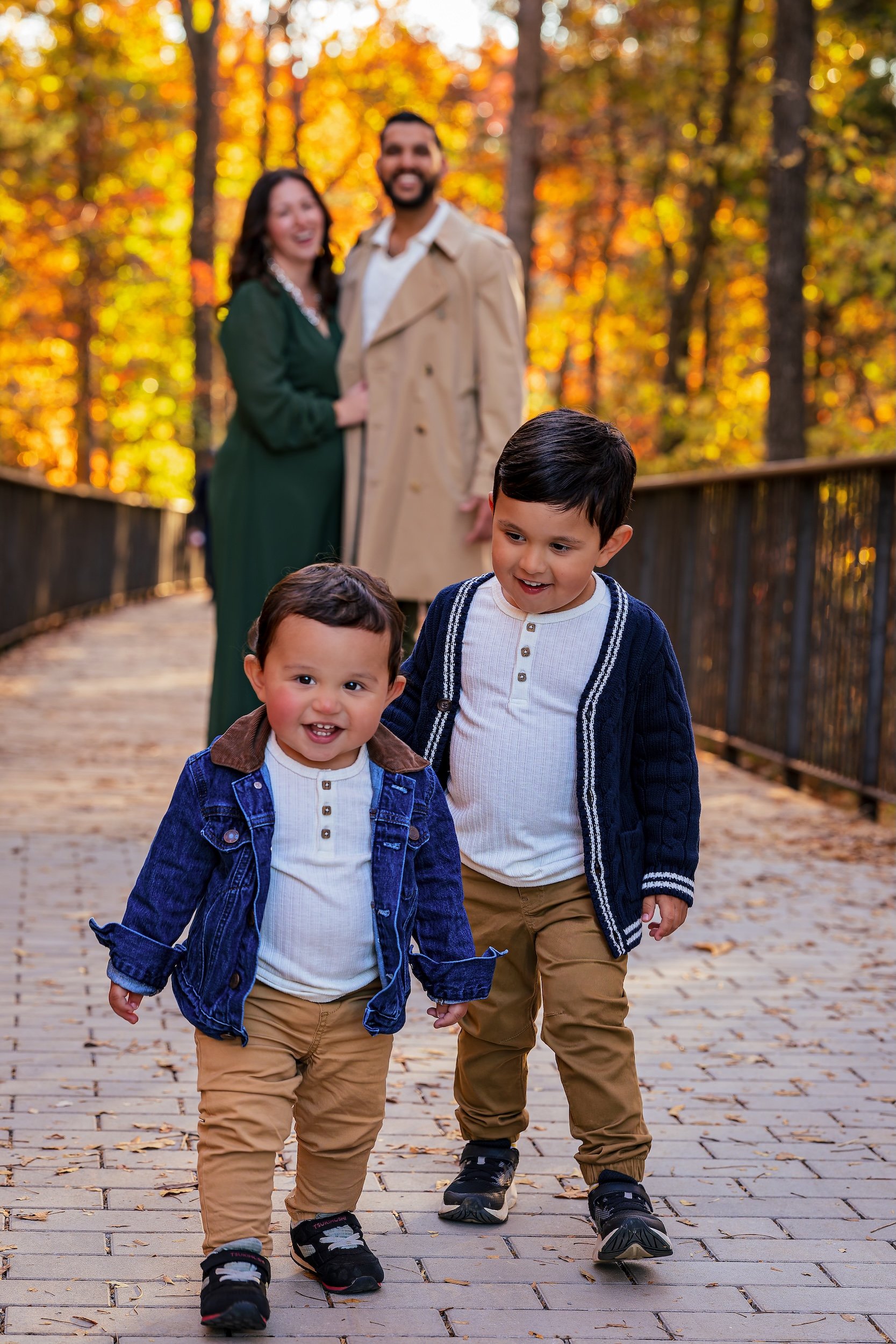 Mom and dad smiling in the background with their two young sons walking and smiling in the forefront of the shot