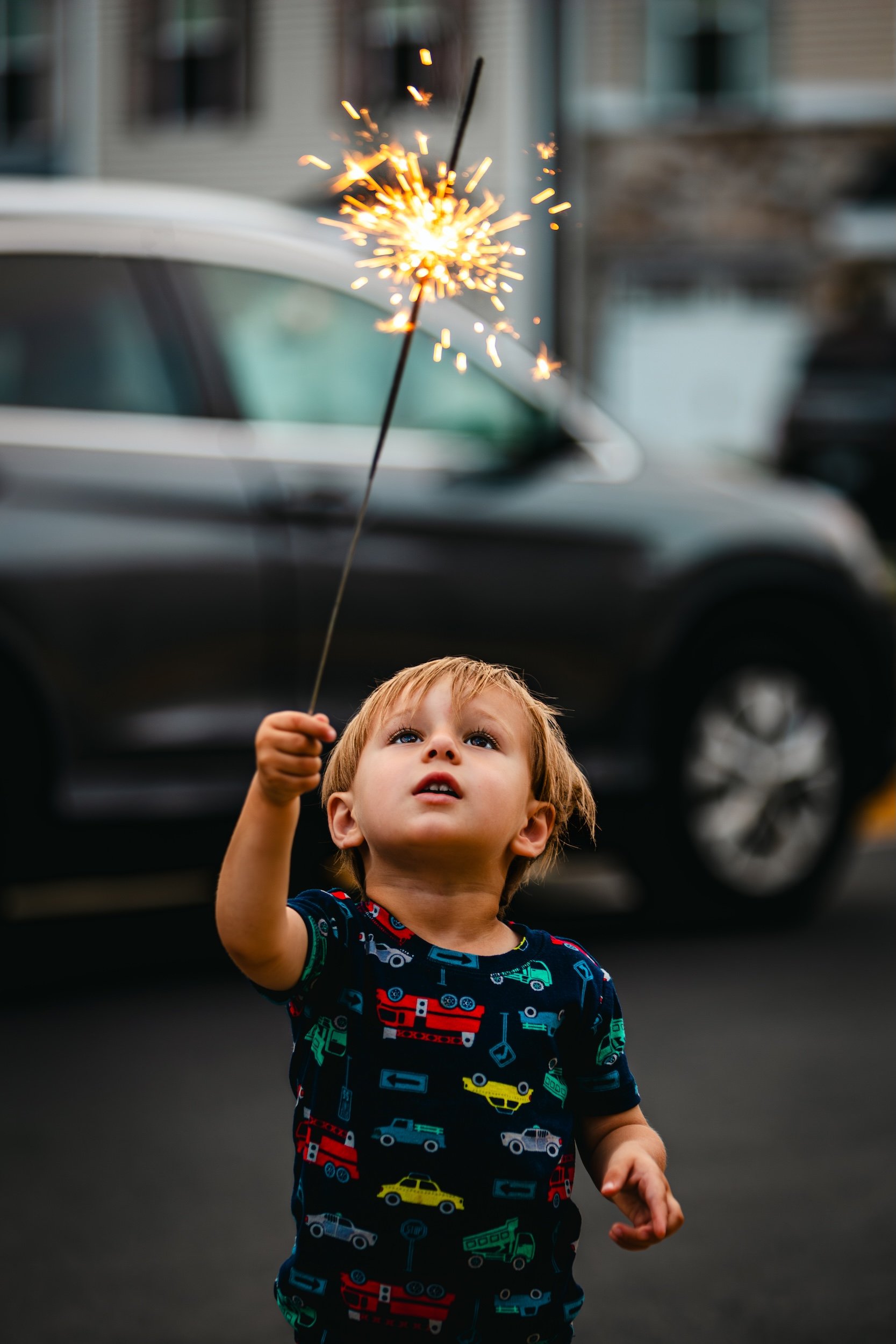 Young boy looking up at a lit sparkler he is holding over the fourth of July