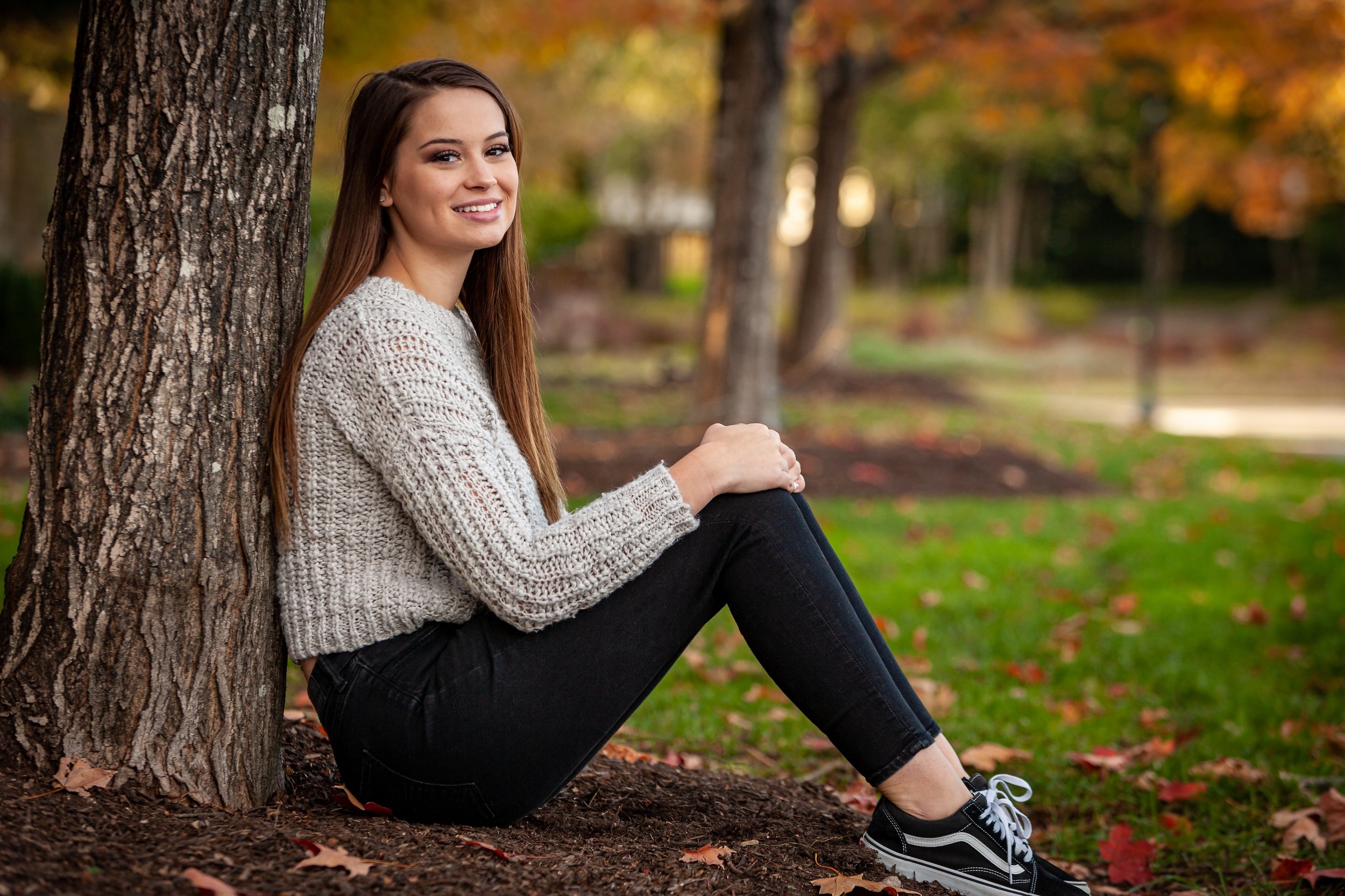 Senior posing for graduation photos sitting underneath a tree