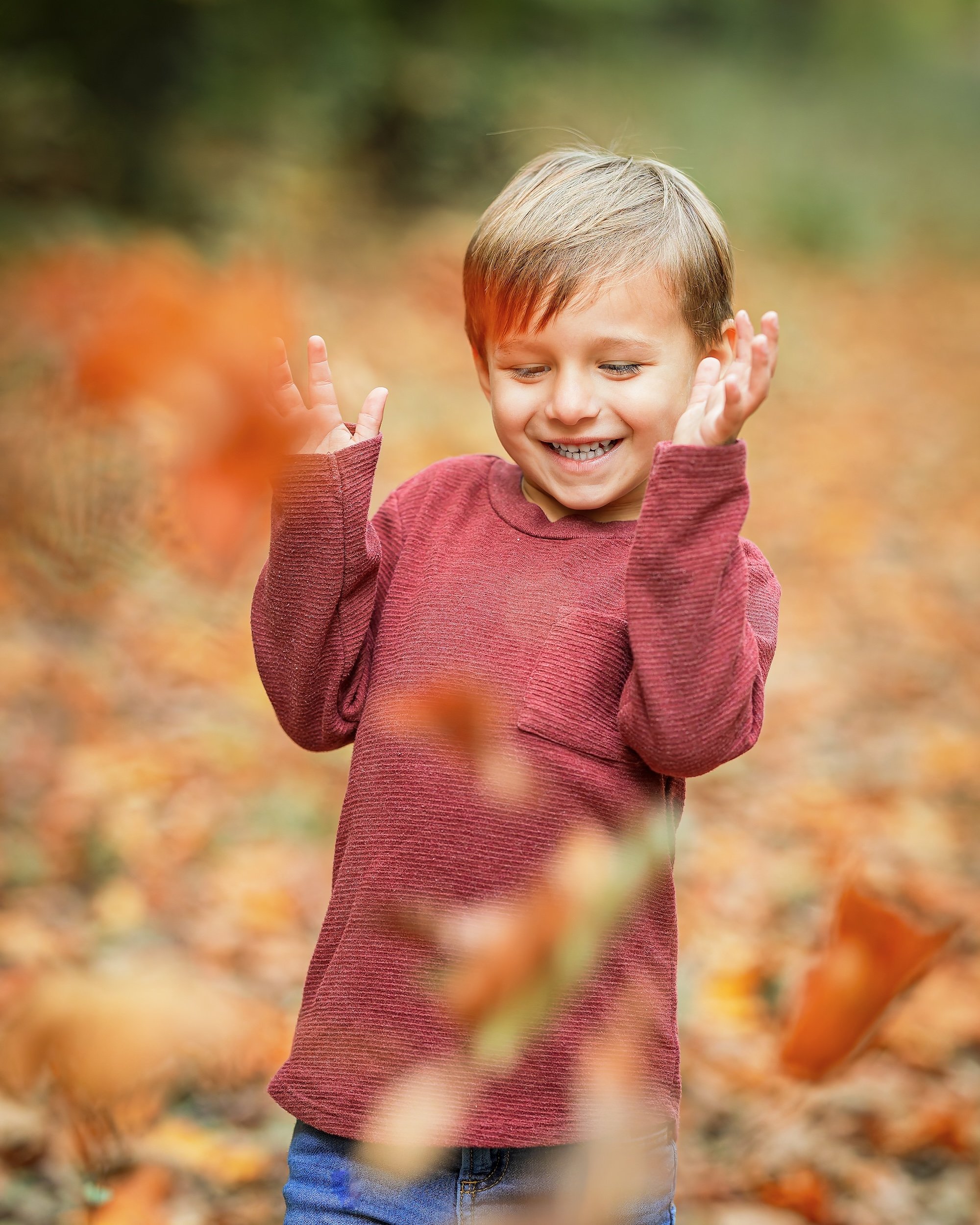 Young boy smiling and playing with fallen leaves