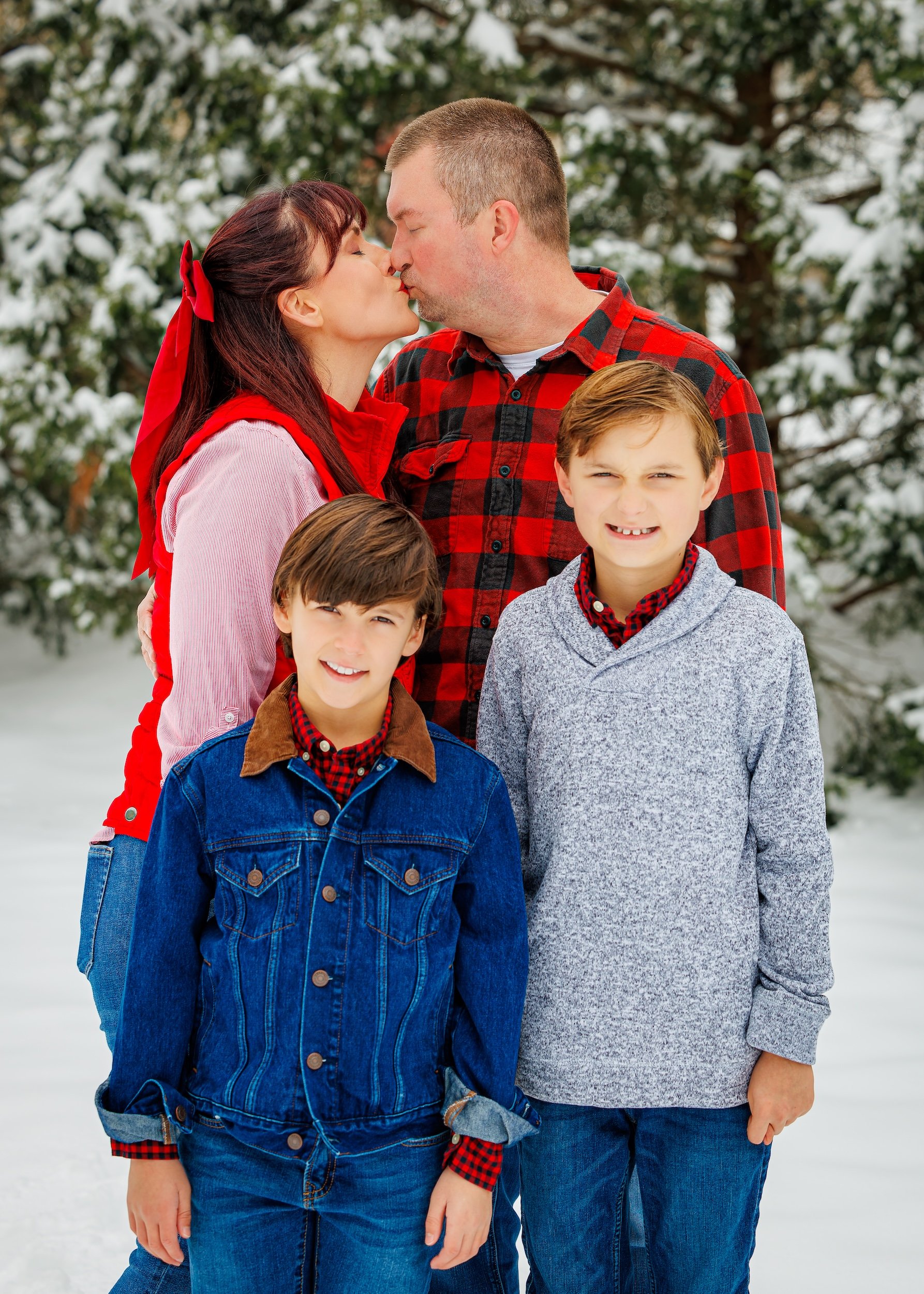 Newly engaged couple kissing in the background with their two sons smiling in the foreground