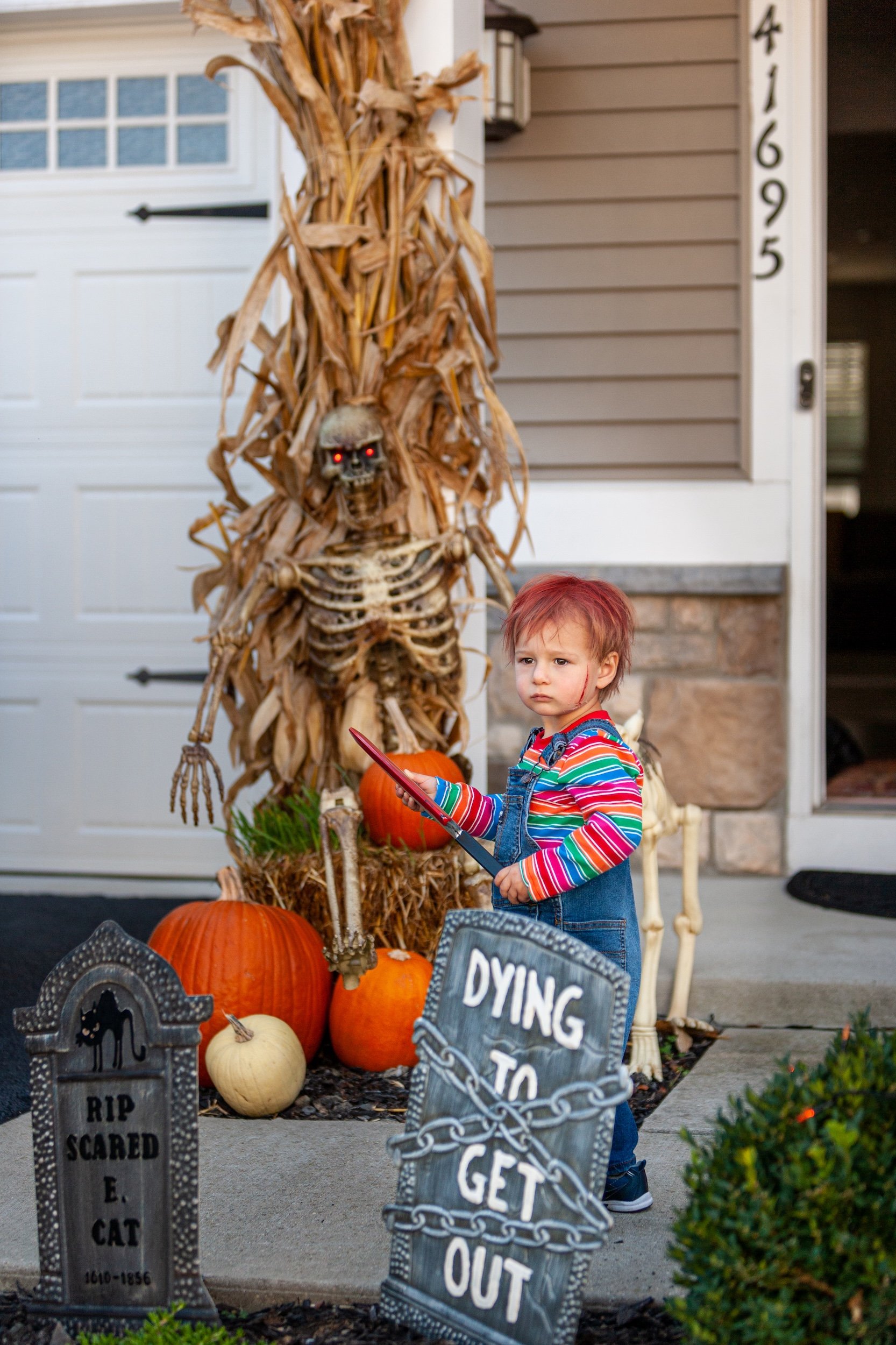 Young boy in Chucky Halloween costume with Halloween decor outside of his home