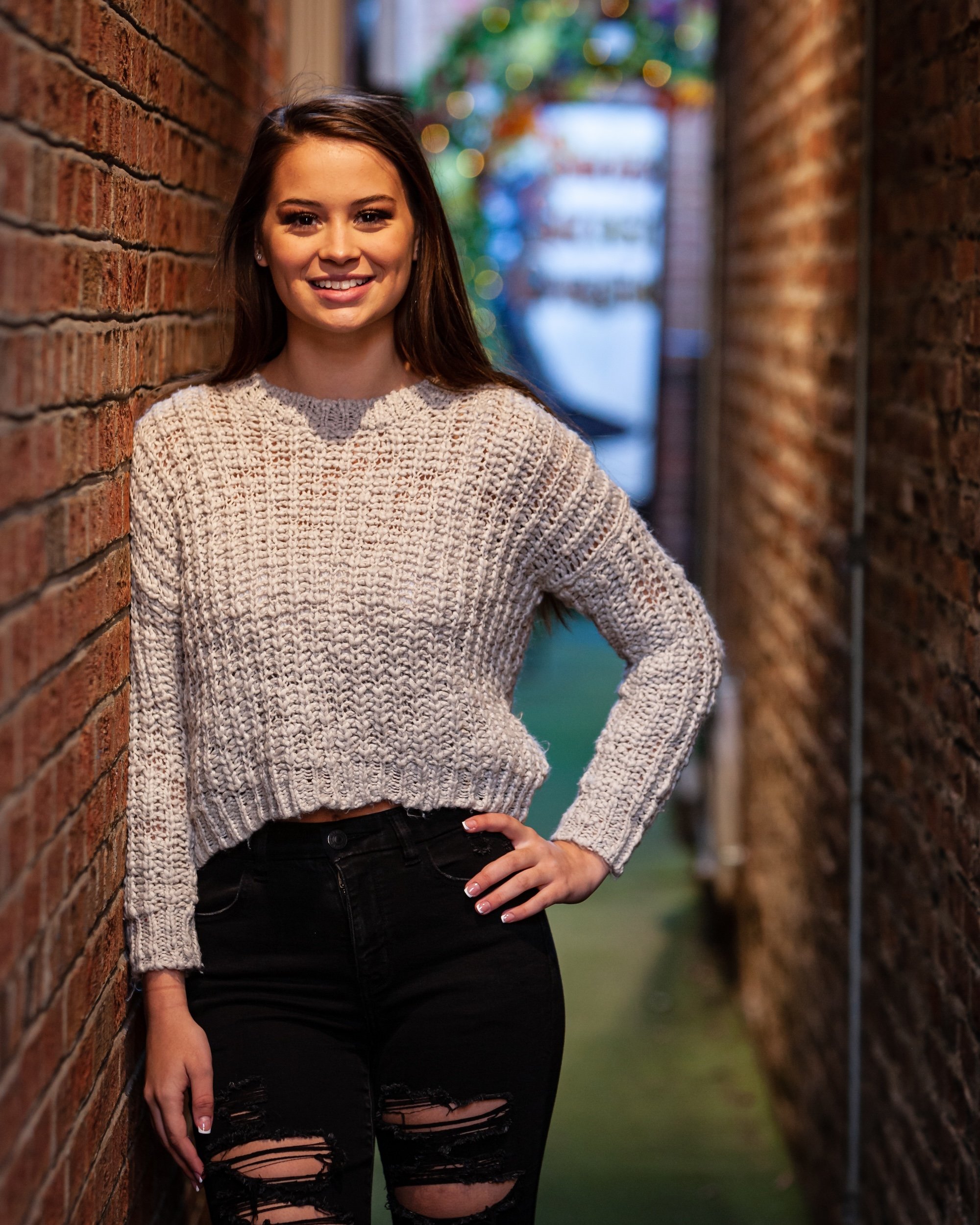 Senior posing for graduation photos in a hallway with two brick walls