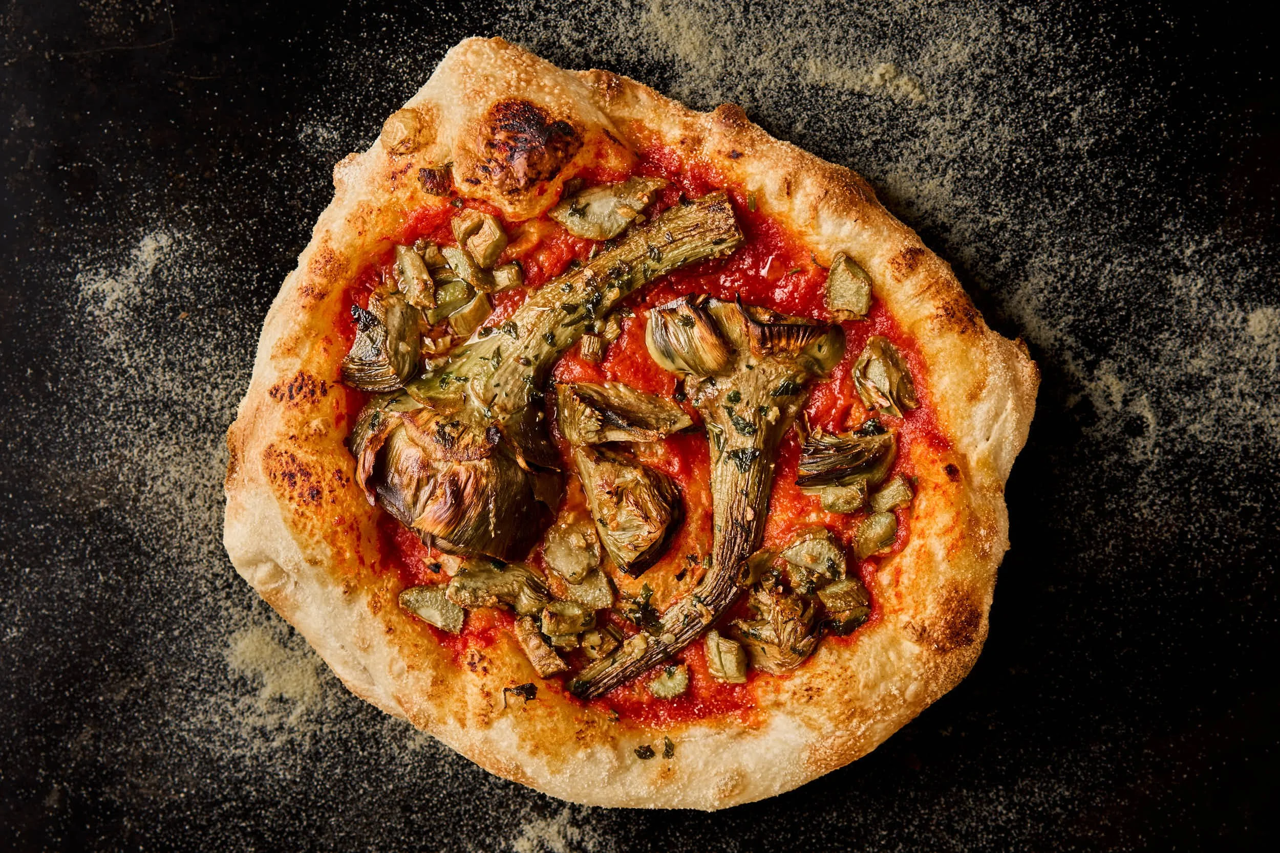 Pizza mit Artischocken auf einem schwarzen Hintergrund mit Mehl