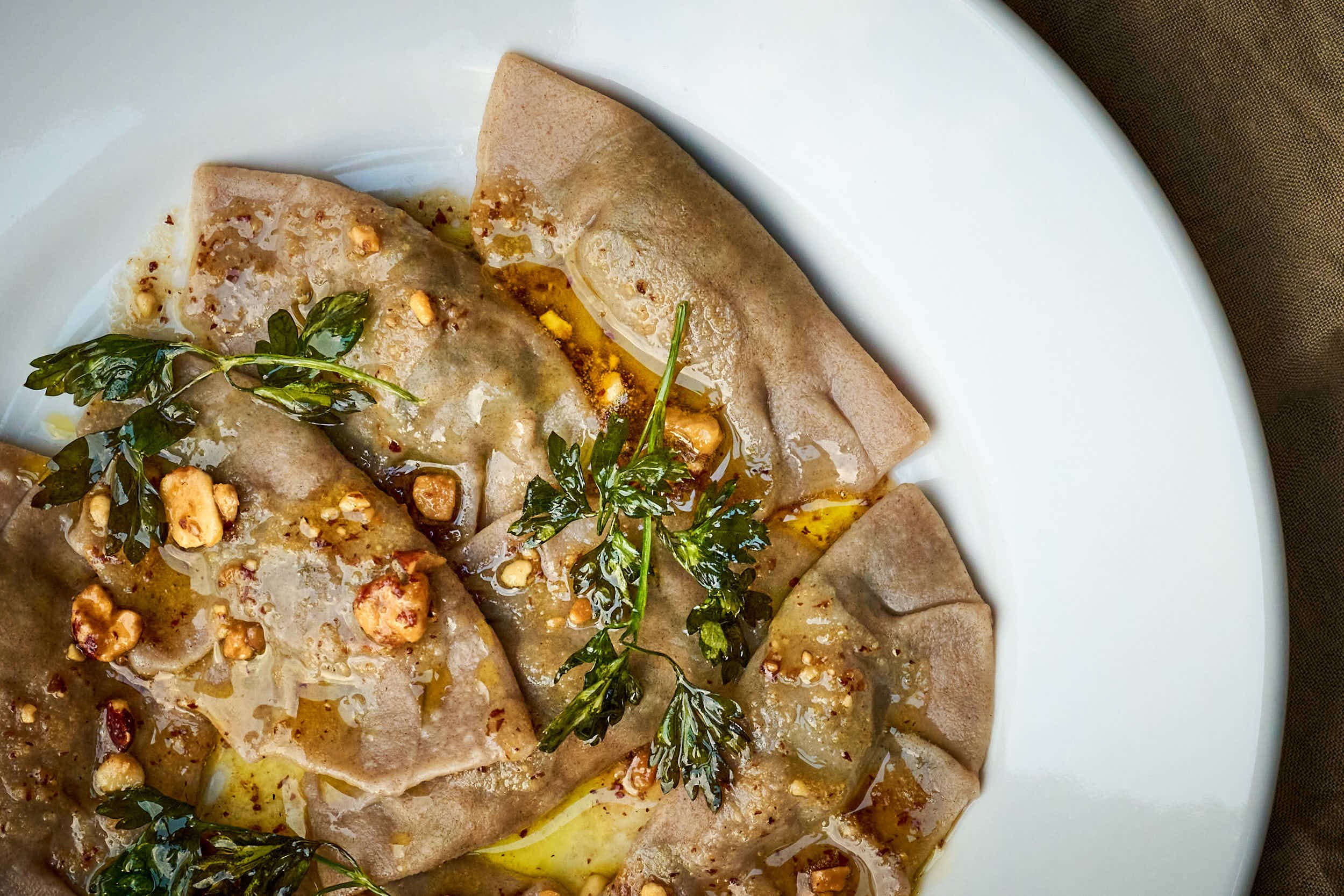 Gericht mit gefüllten Teigtaschen, garniert mit frischen Kräutern, roter Pfefferflocken und Nüssen, auf weißem Teller serviert.