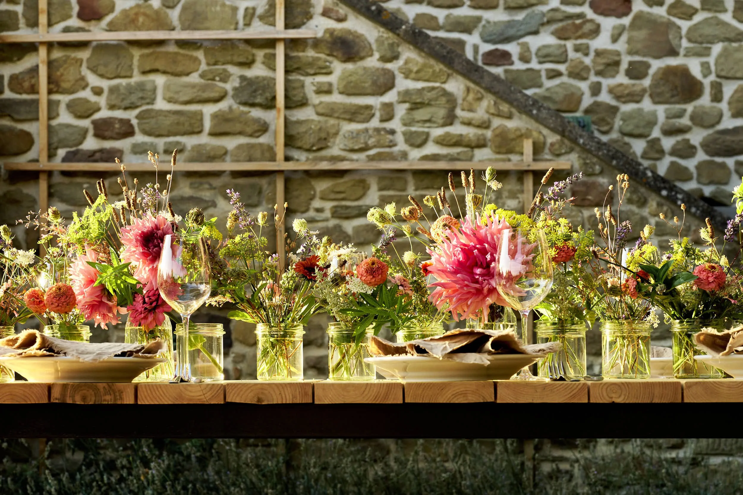 Blumenarrangement in Gläsern auf einem Holztisch mit einem steinernen Hintergrund.