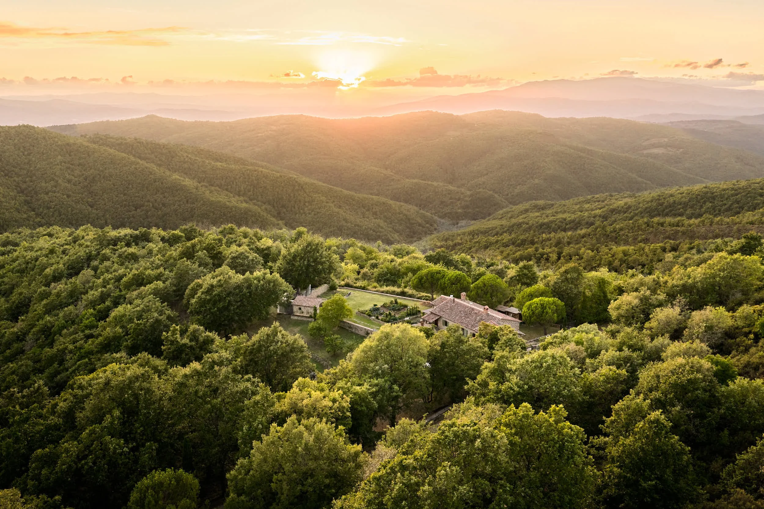 Ein Haus inmitten eines dichten Waldes bei Sonnenuntergang in einer bergigen Landschaft.