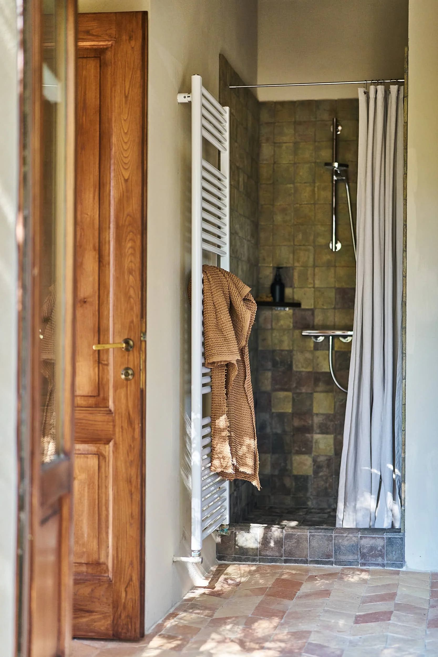 Badezimmer mit offener Dusche, weißen Handtuchheizkörper und Holztür.