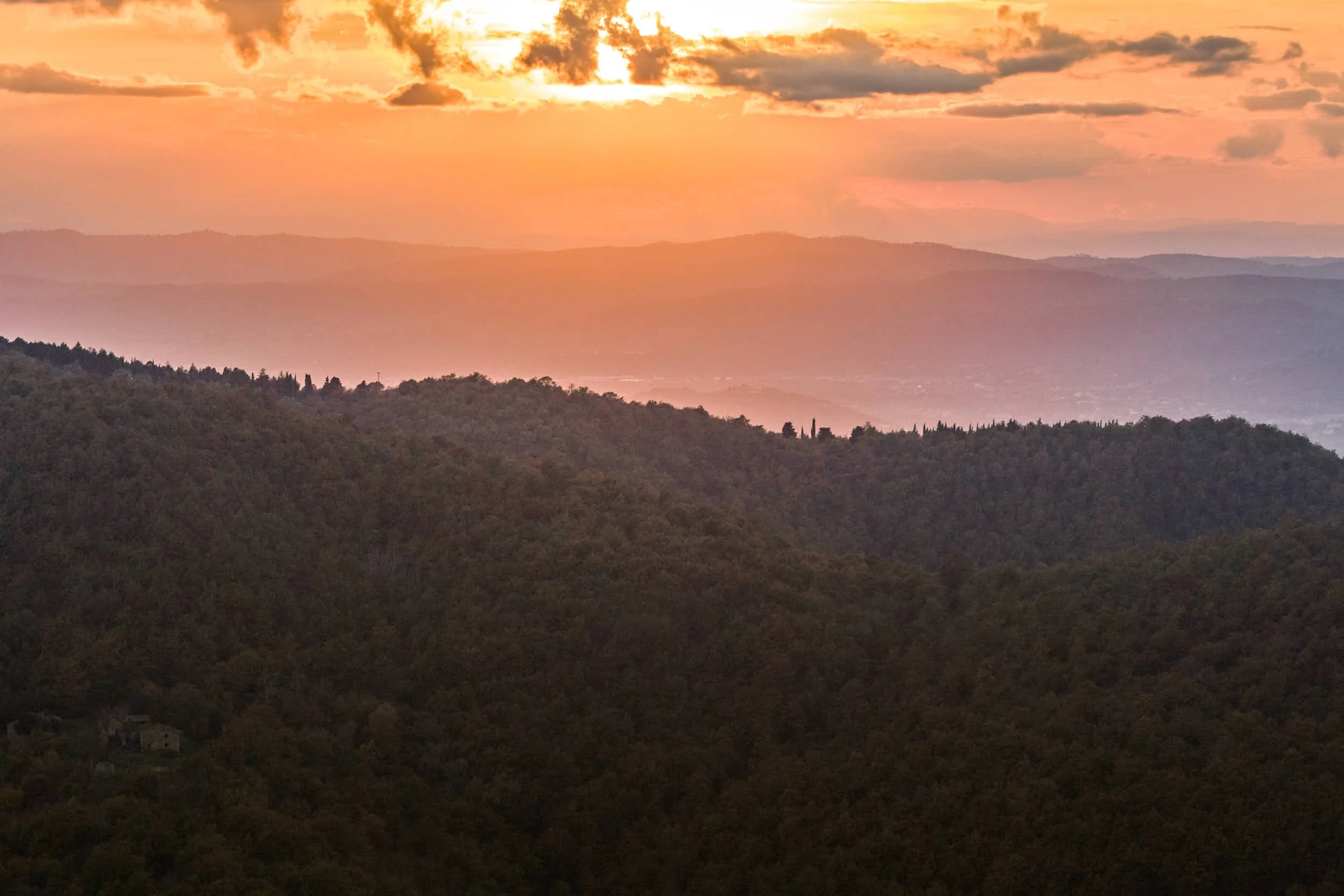 Blick auf eine hügelige Landschaft bei Sonnenuntergang mit einem orangefarbenen Himmel und Wolken