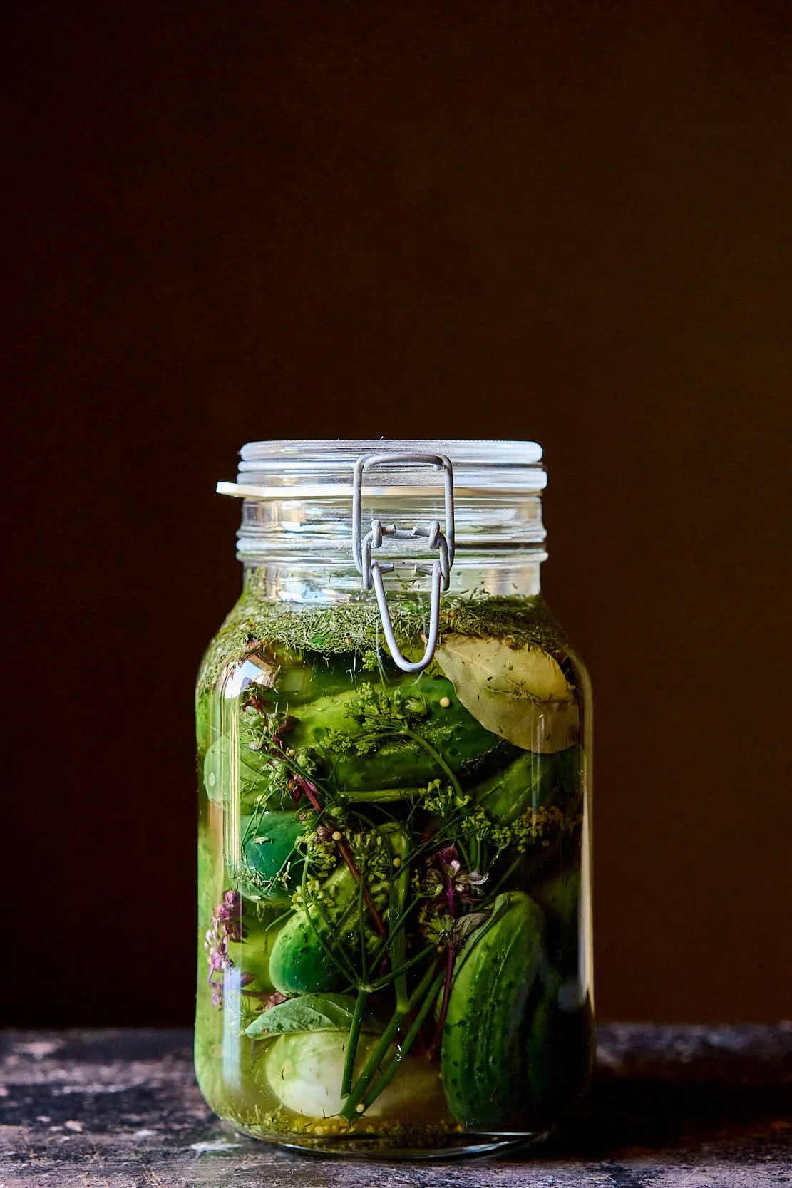 Ein Glas mit eingelegtem Gemüse und Kräutern, verschlossen mit einem Metallverschluss, auf einem Holztisch.