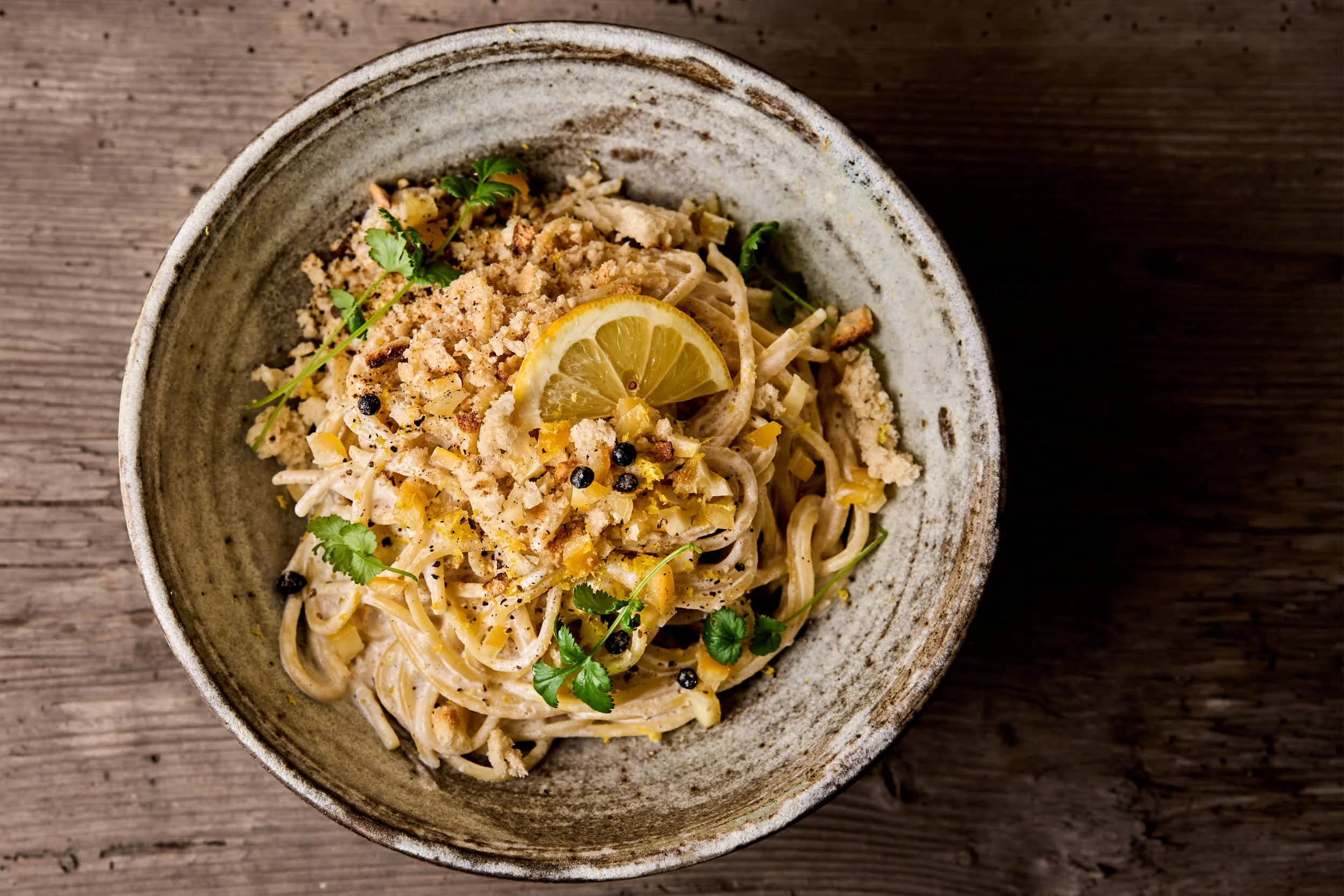 Eine Schale mit Pasta, garniert mit Zitronenscheiben, Kräutern und Gewürzen, auf einem Holztisch