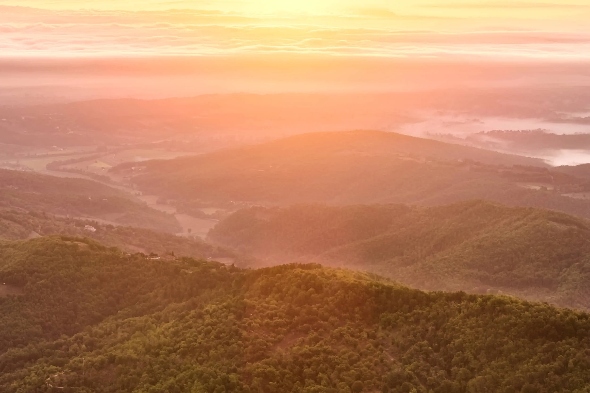 Landschaft mit Bergen im Sonnenaufgang, Himmel in warmen Orangetönen, bewölkter Himmel