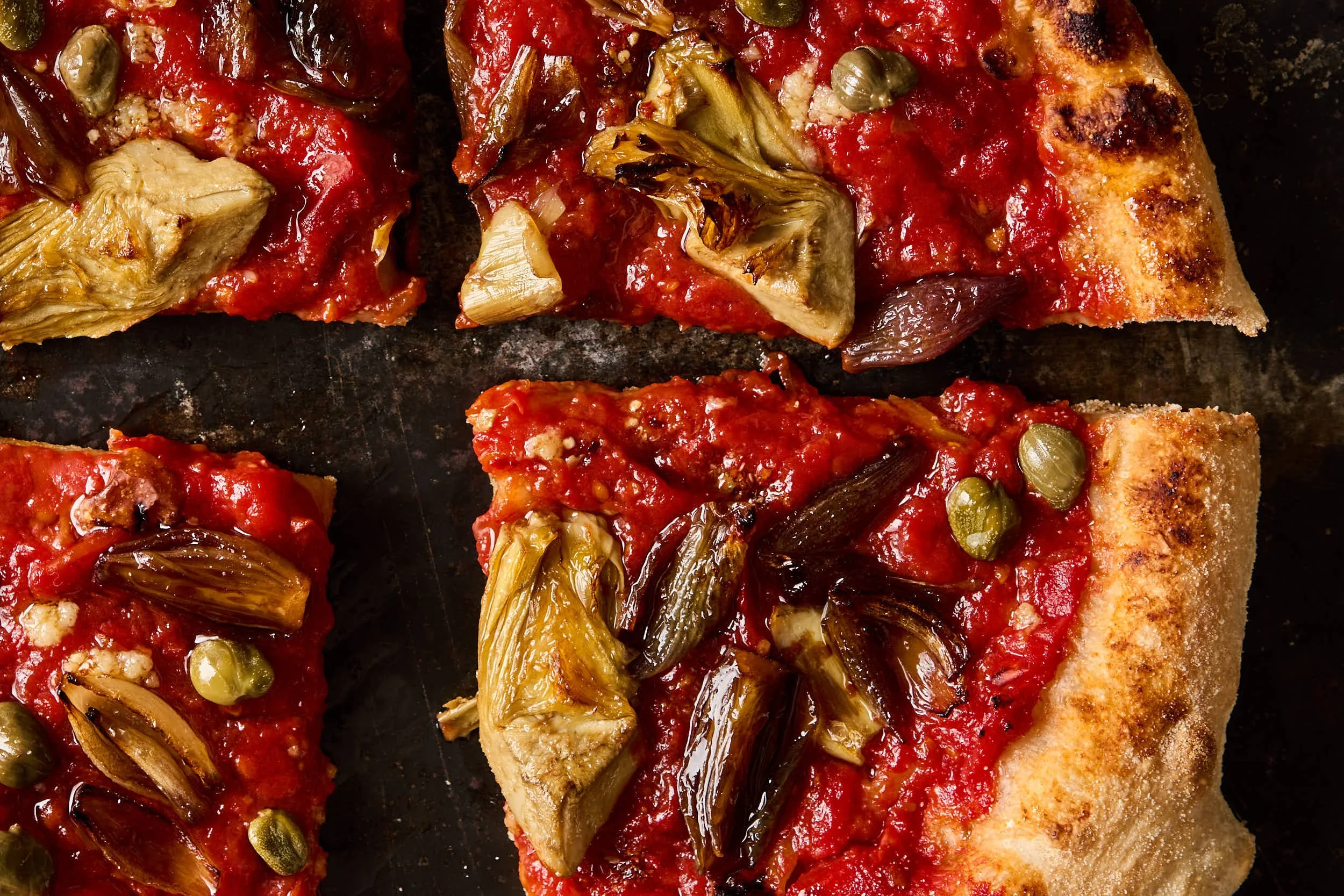 Pizzastücke mit Artischocken, Kapern, Tomatensoße und gegrilltem Boden