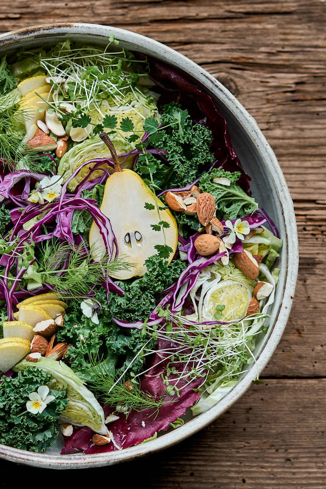 Gemischter Salat mit Birne, Rotkohl, Grünkohl, Kresse, diverse Nüsse und essbare Blüten in einer Schüssel auf Holz table.