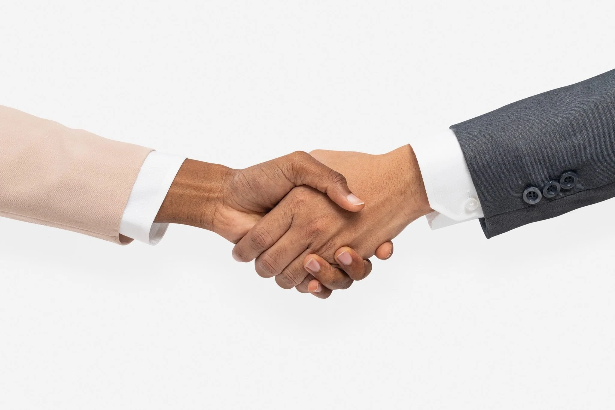 Two people in business attire shaking hands against a plain white background.