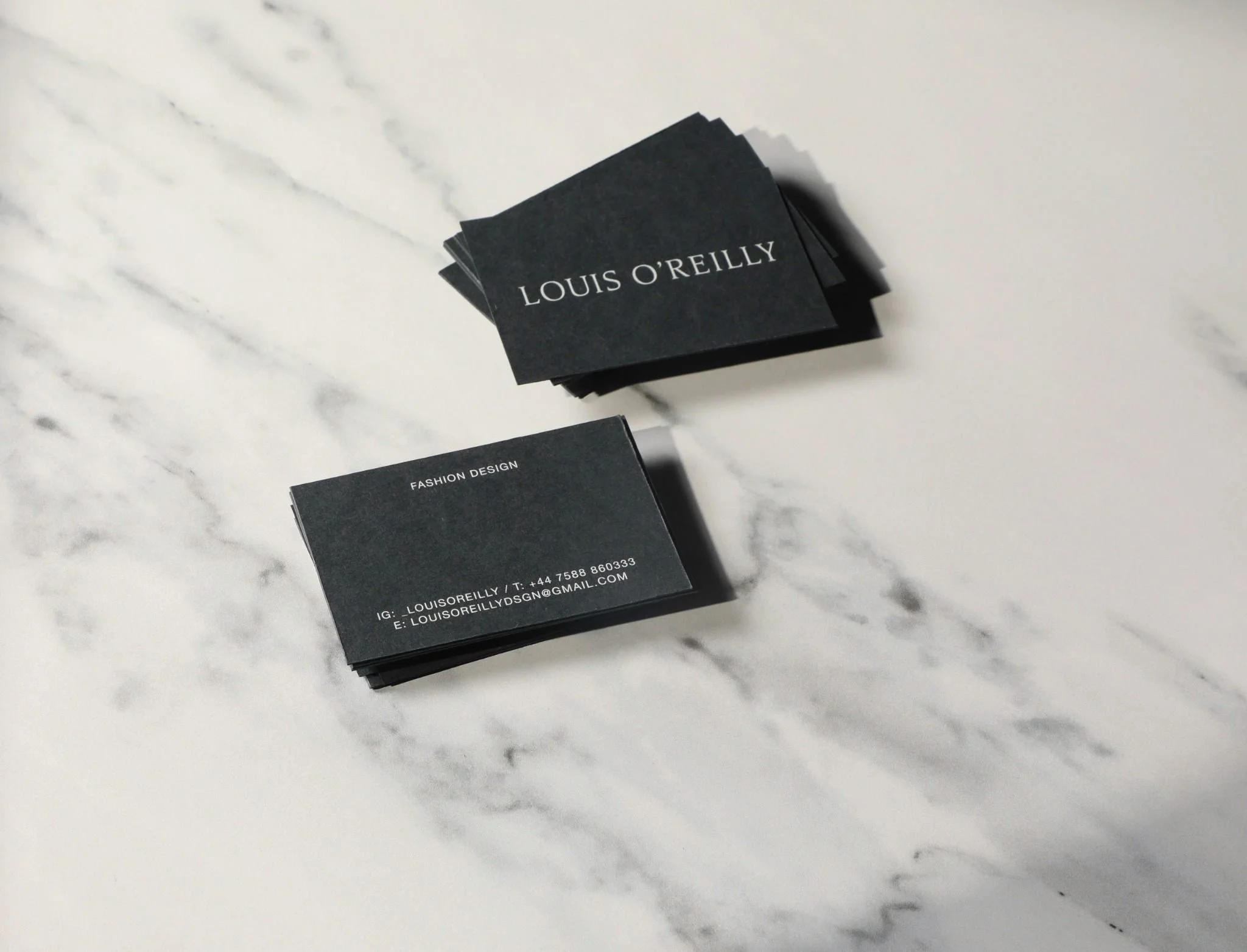 Stacks of black business cards for Louis O'Reilly on white marble surface.