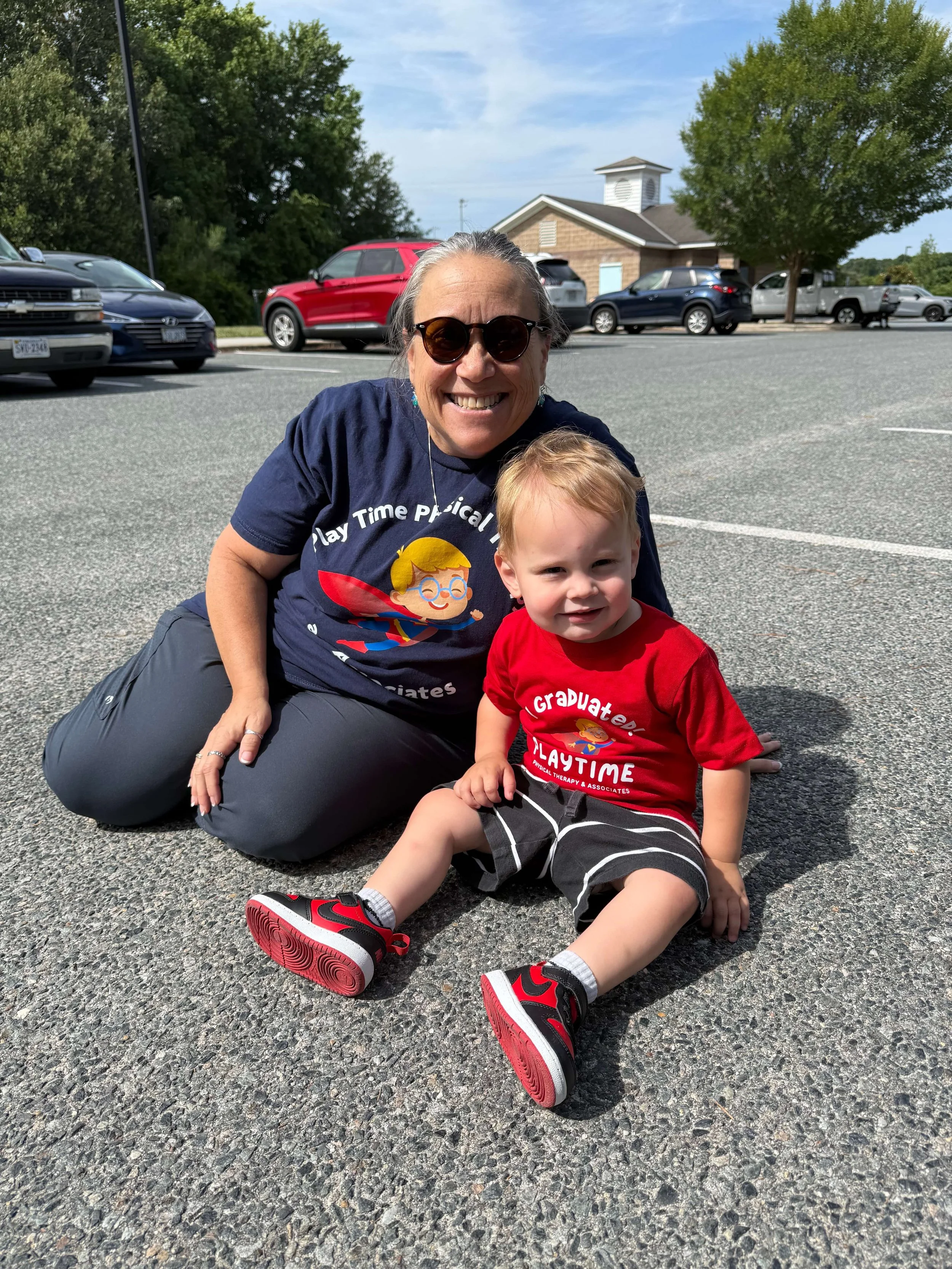  Dr. Rose and Jackson sitting together on the pavement and smiling. 