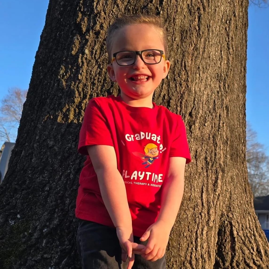 smiling little boy with playtime shirt that says “I graduated”